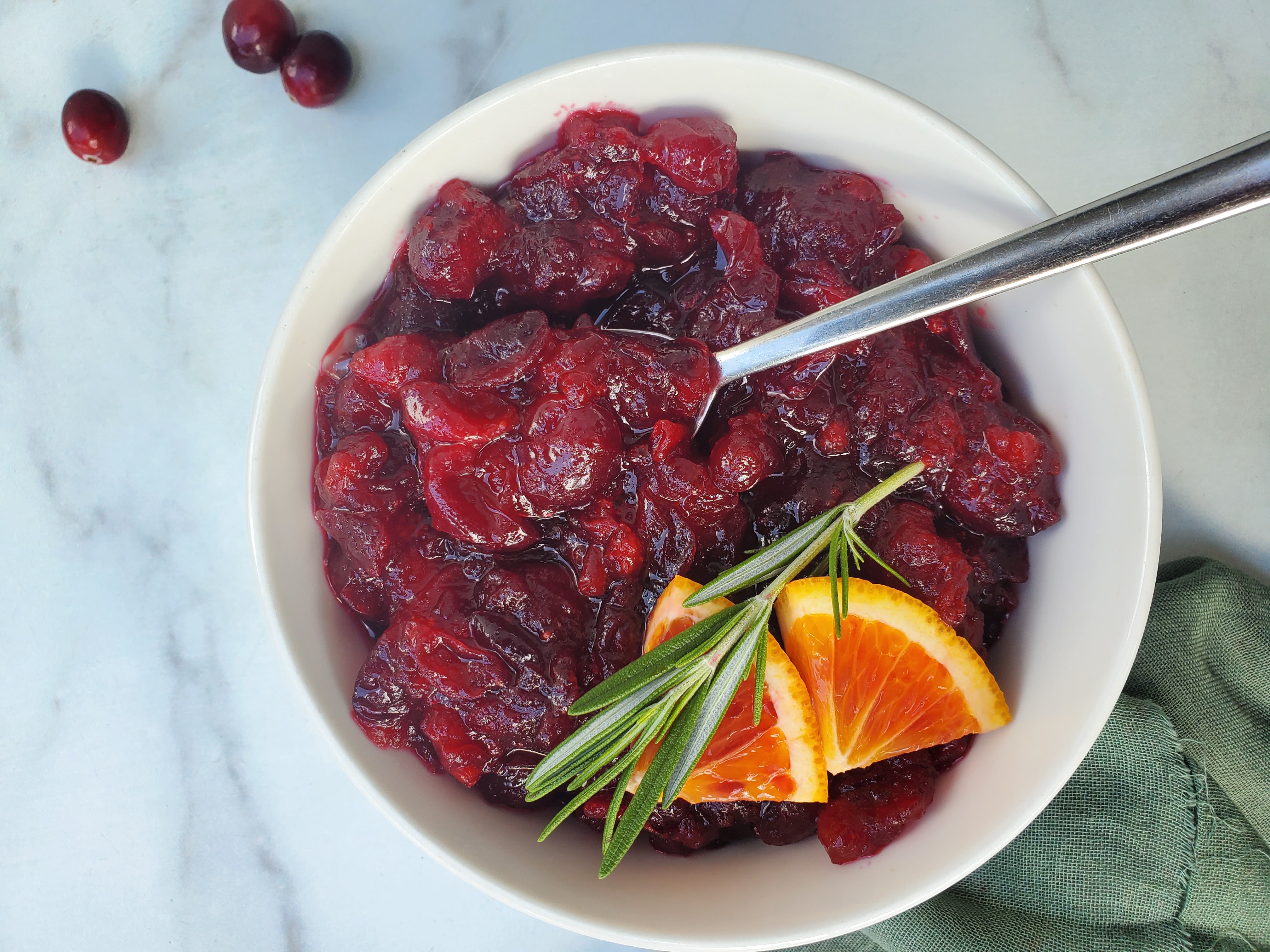 Cranberry Sauce in a bowl with orange wedges and rosemary