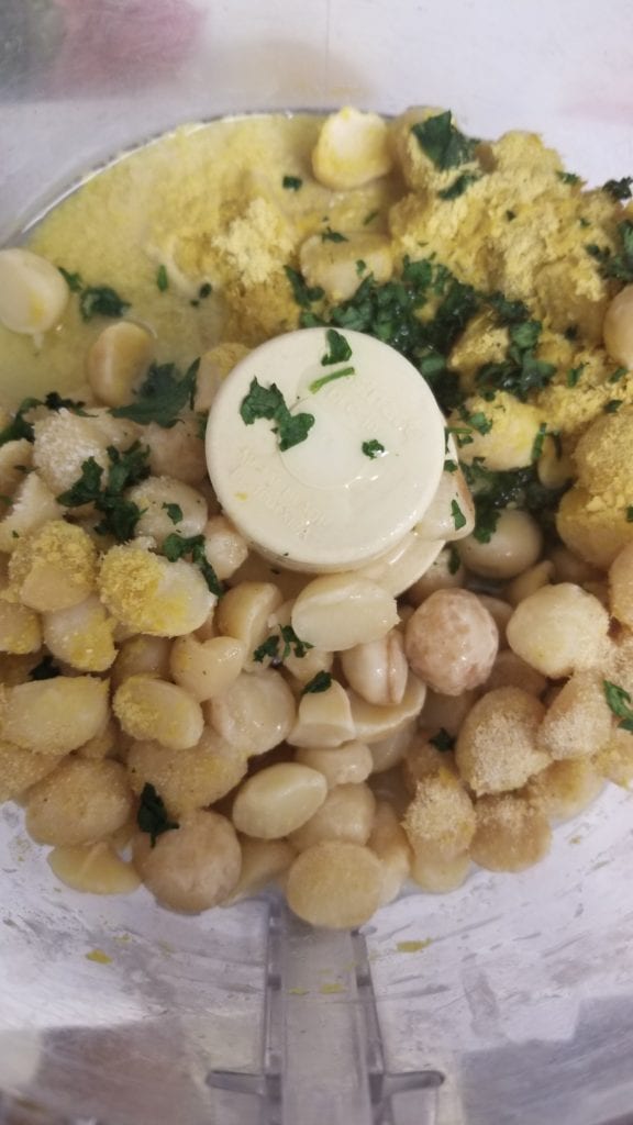 food processor bowl with macadamia nuts, nutritional yeast, lemon juice, garlic powder, and water