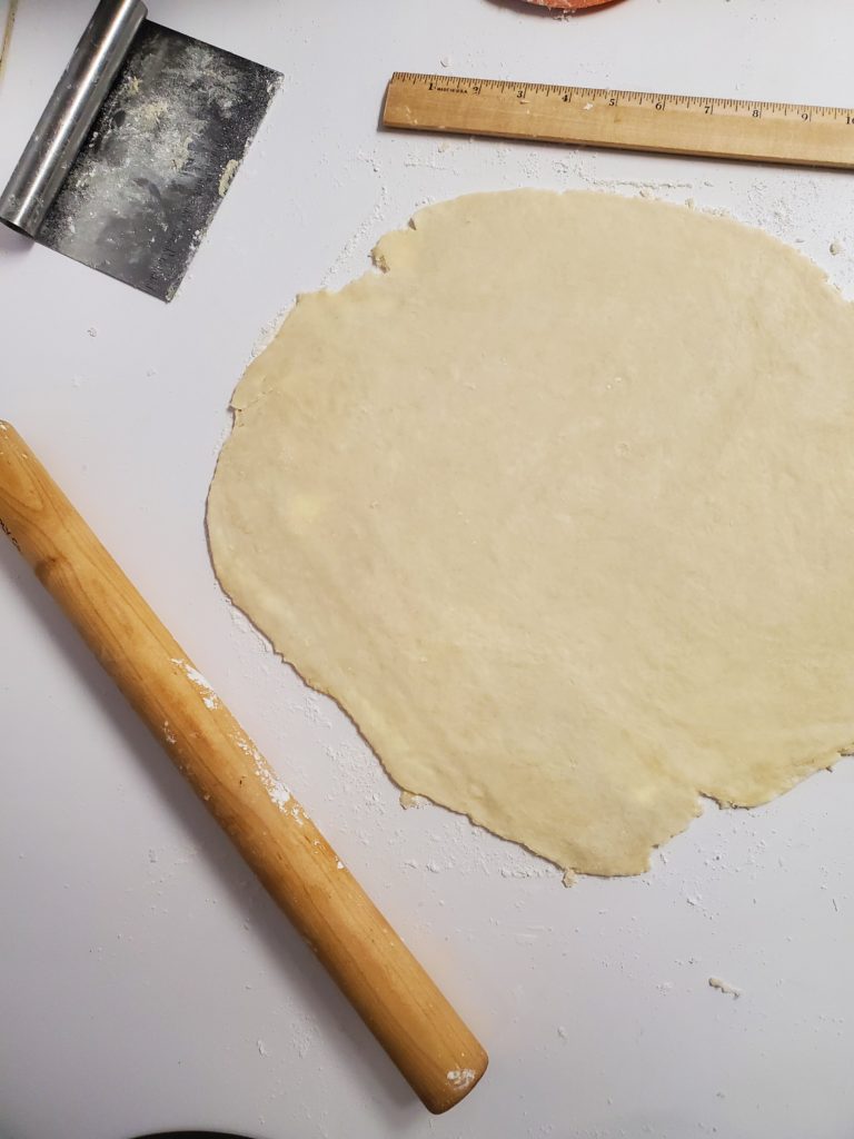 pie dough rolled out with a rolling pin, bench scraper, and a ruler