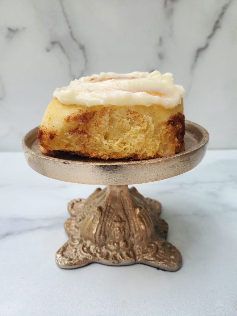 cinnamon roll on a pedestal with cream cheese frosting