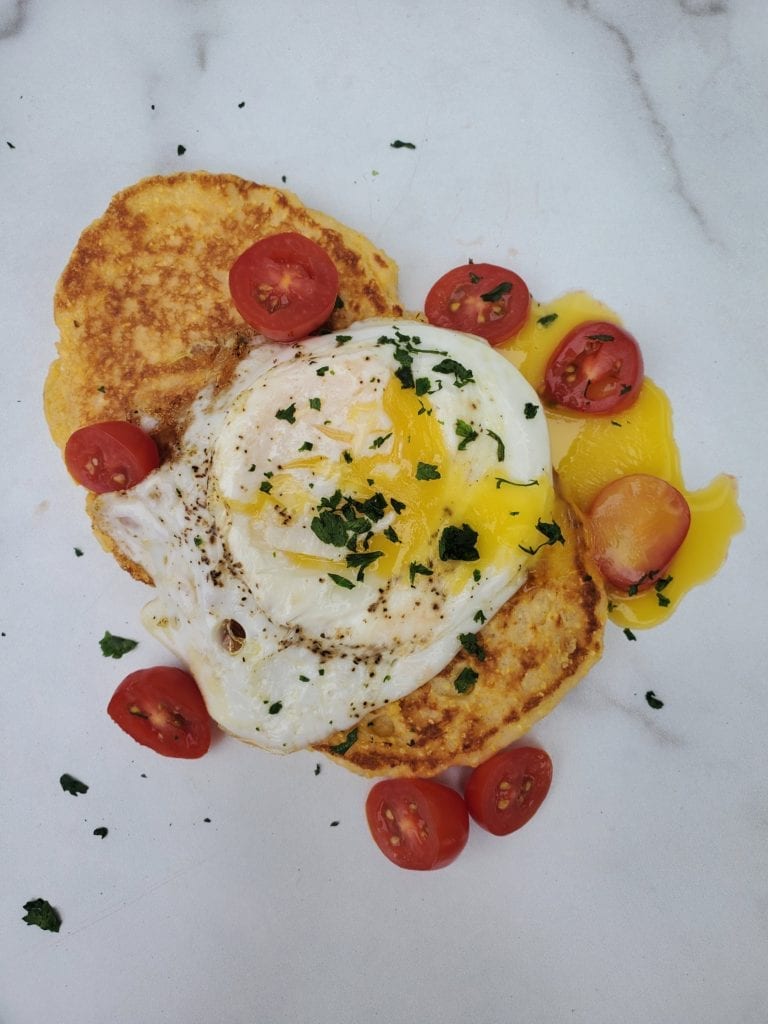 2 Johnnie Cakes with runny eggs on top and sliced tomatoes