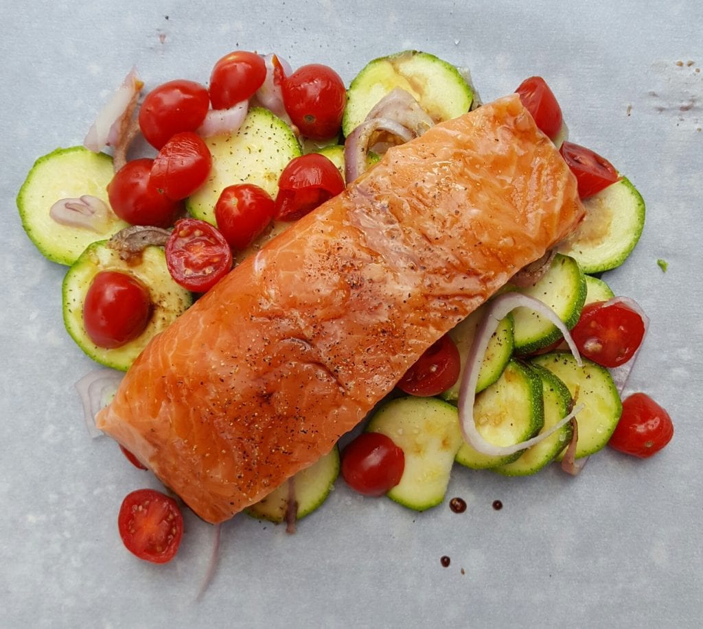 salmon sitting on top of zucchini, shallots, and tomatoes