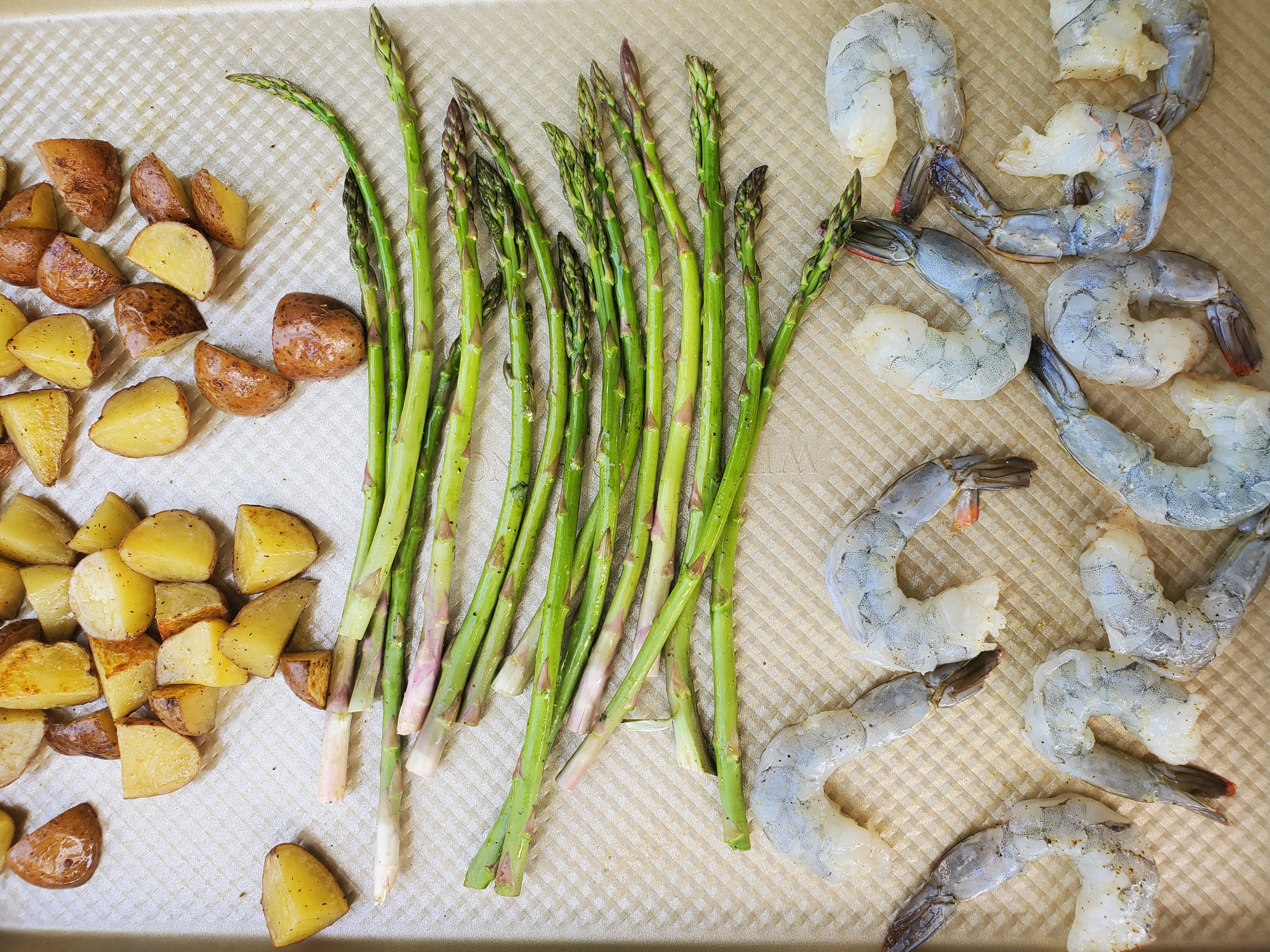 Sheet pan with the cut up potatoes partially cooked and now adding asparagus and shrimp to cook