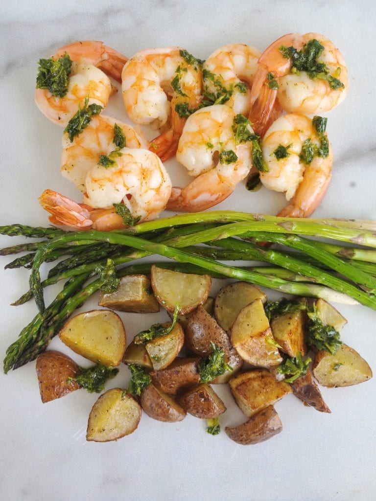 Finished sheet pan dinner - roasted shrimp, asparagus, and potatoes with a drizzle of chimichurri