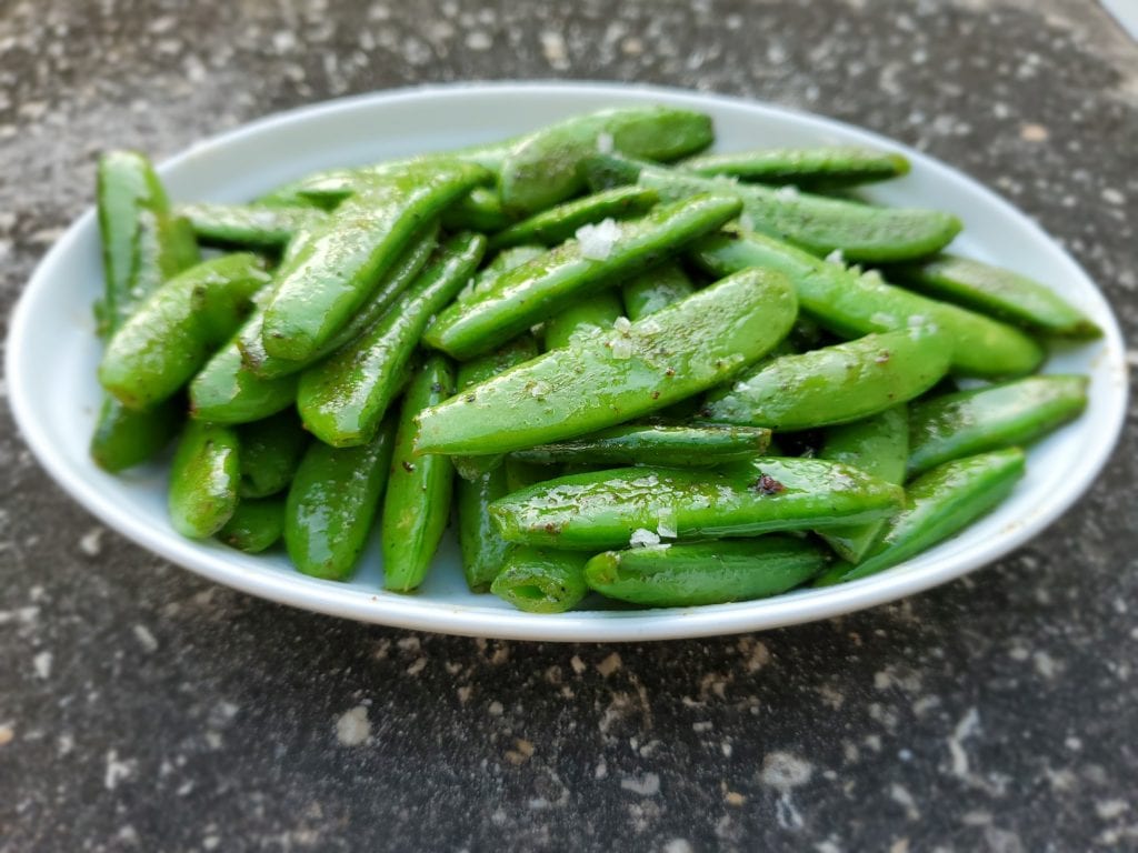 Plate of roasted sugar snap peas with sprinkled black pepper