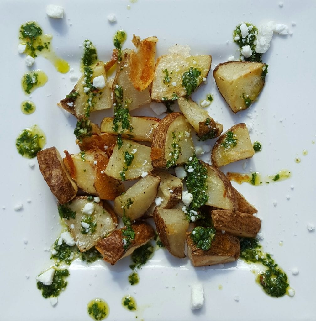 plate of roasted potatoes with chimichurri sauce drizzled on top
