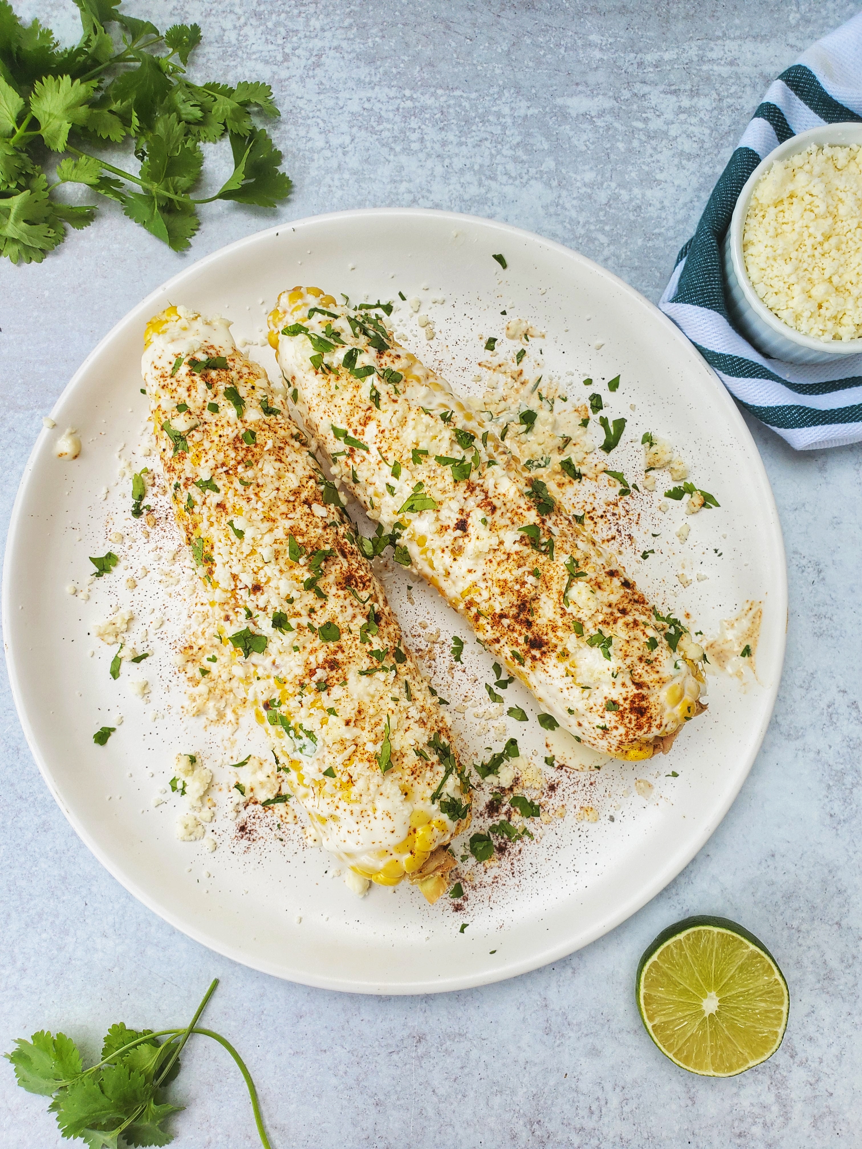 Mexican Street Corn on a plate. Cheese, lime, and cilantro to the side