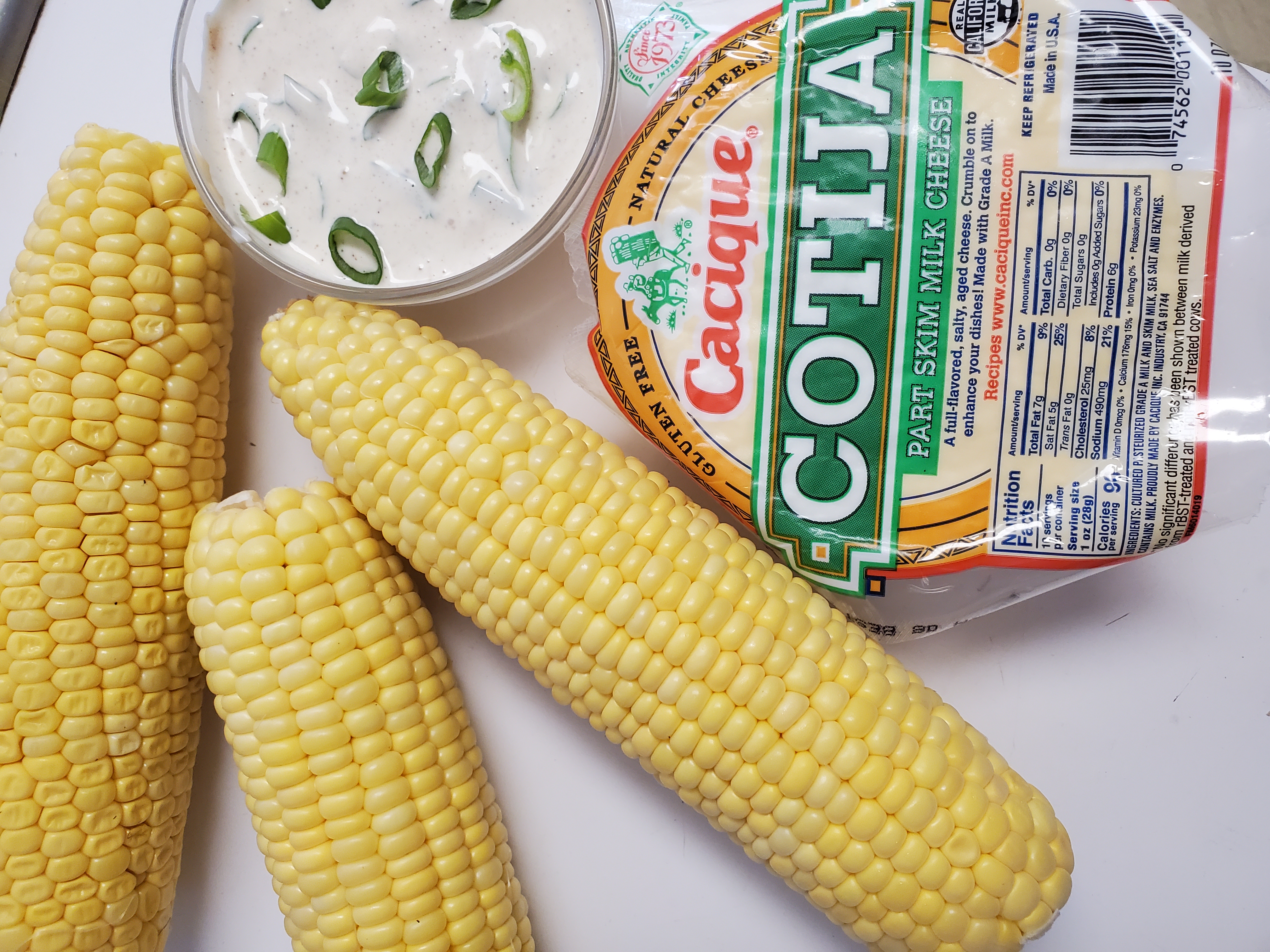 ingredients to make mexican street corn - corn on the cob, cotija cheese, sour cream, mayonnaise, and lime juice