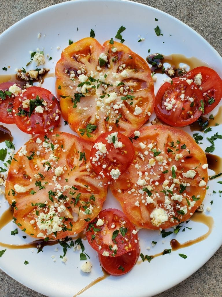 Tomatoes on a plate with blue cheese and herbs with a balsamic drizzle
