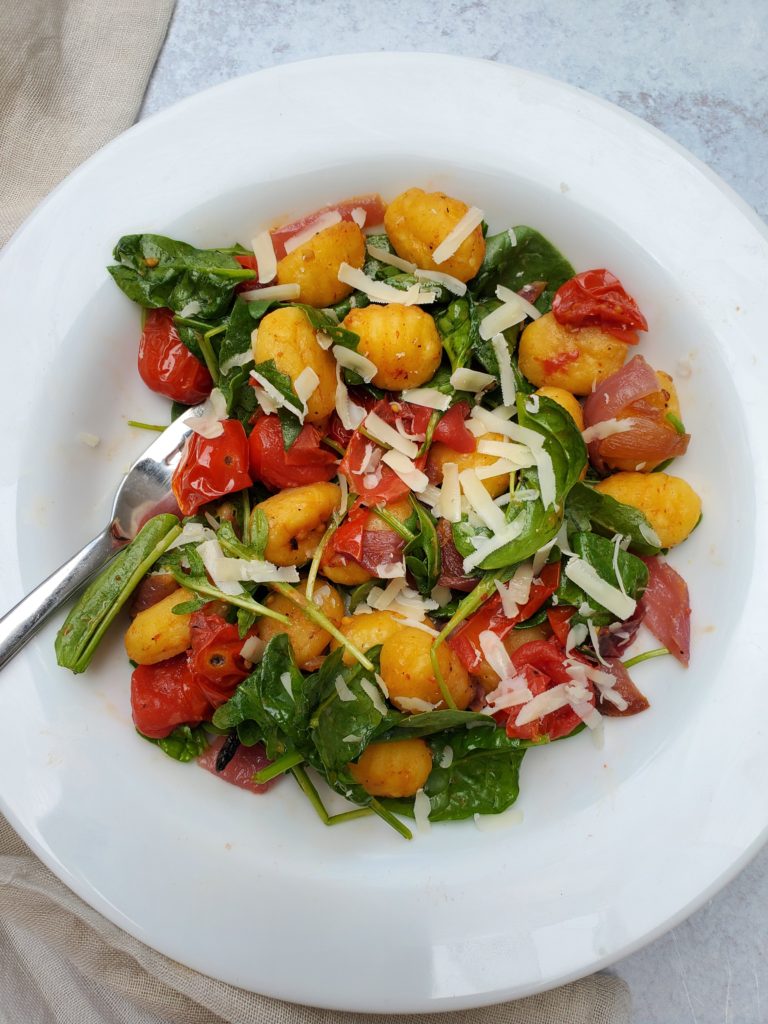 Gnocchi, Roasted Tomatoes & Onions, Wilted Arugula, & Shaved Parmesan in a bowl
