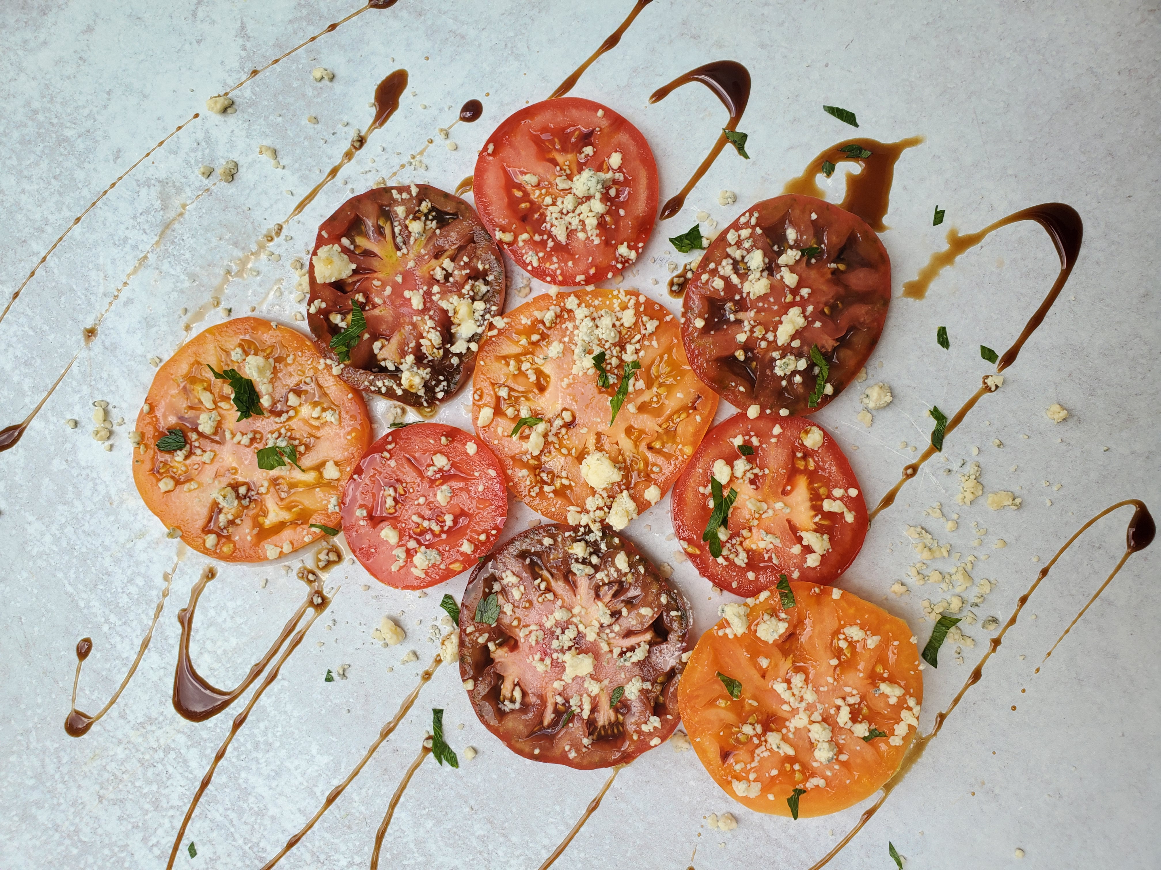 Heirloom Tomatoes sliced with cheese crumbled on top and balsamic glaze drizzled on top