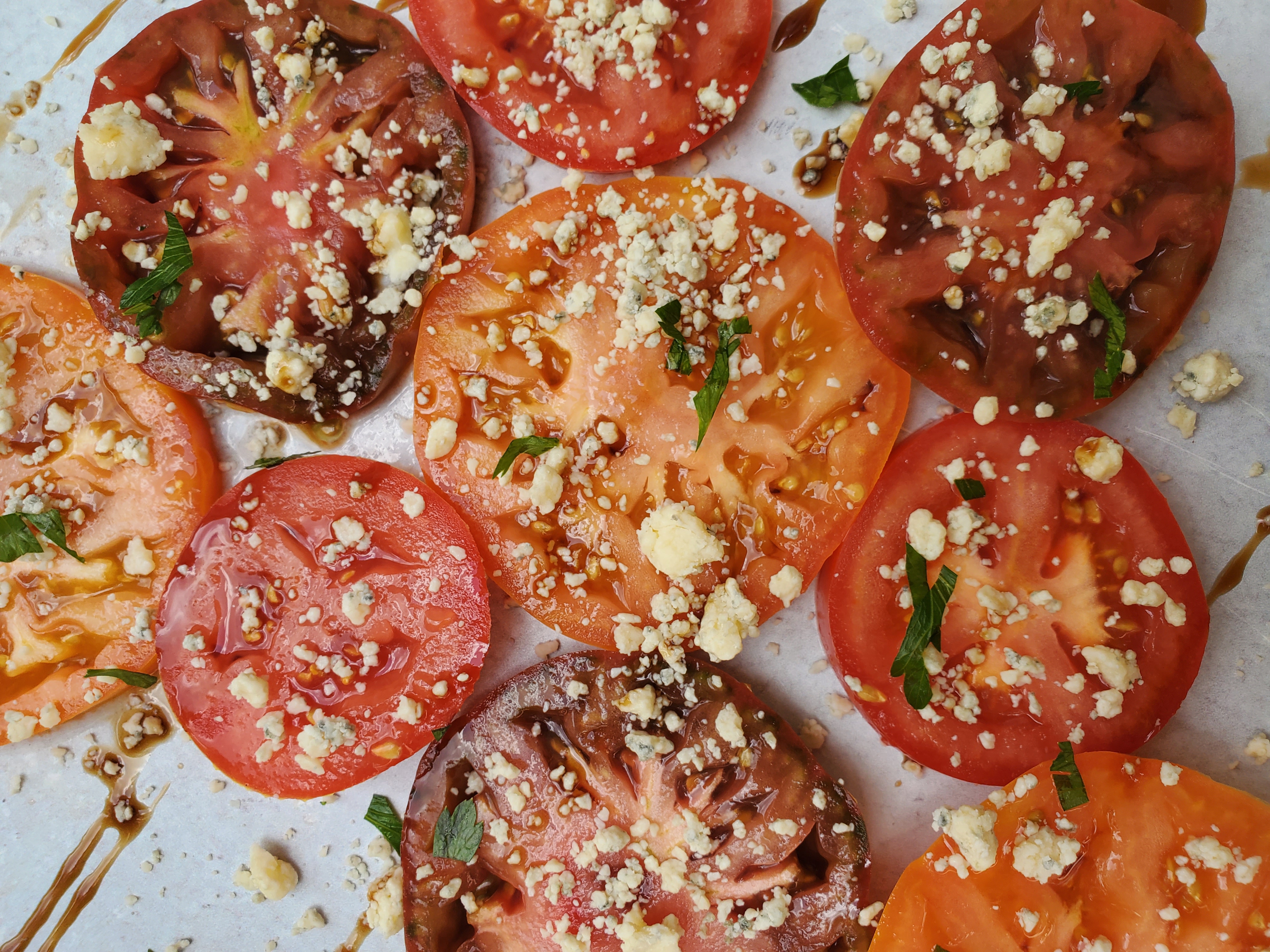 Up-close shot of heirloom tomatoes, topped with blue cheese and drizzled with balsamic glaze