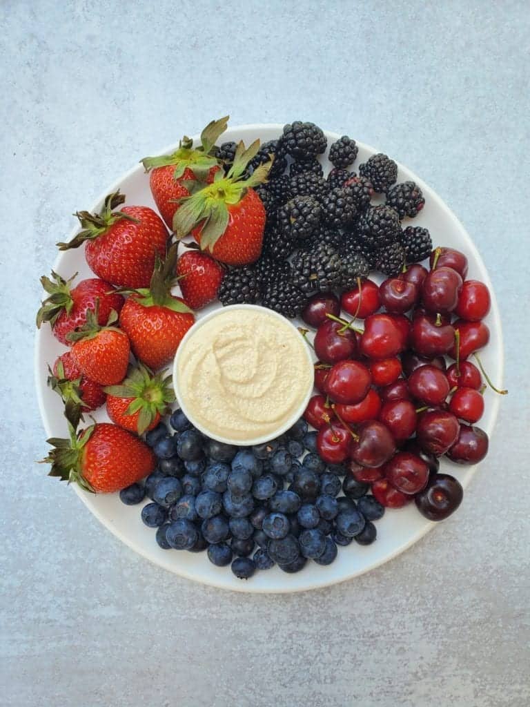 Cashew sweet cream in a bowl in the center of a plate surrounded by fruit to dip into it