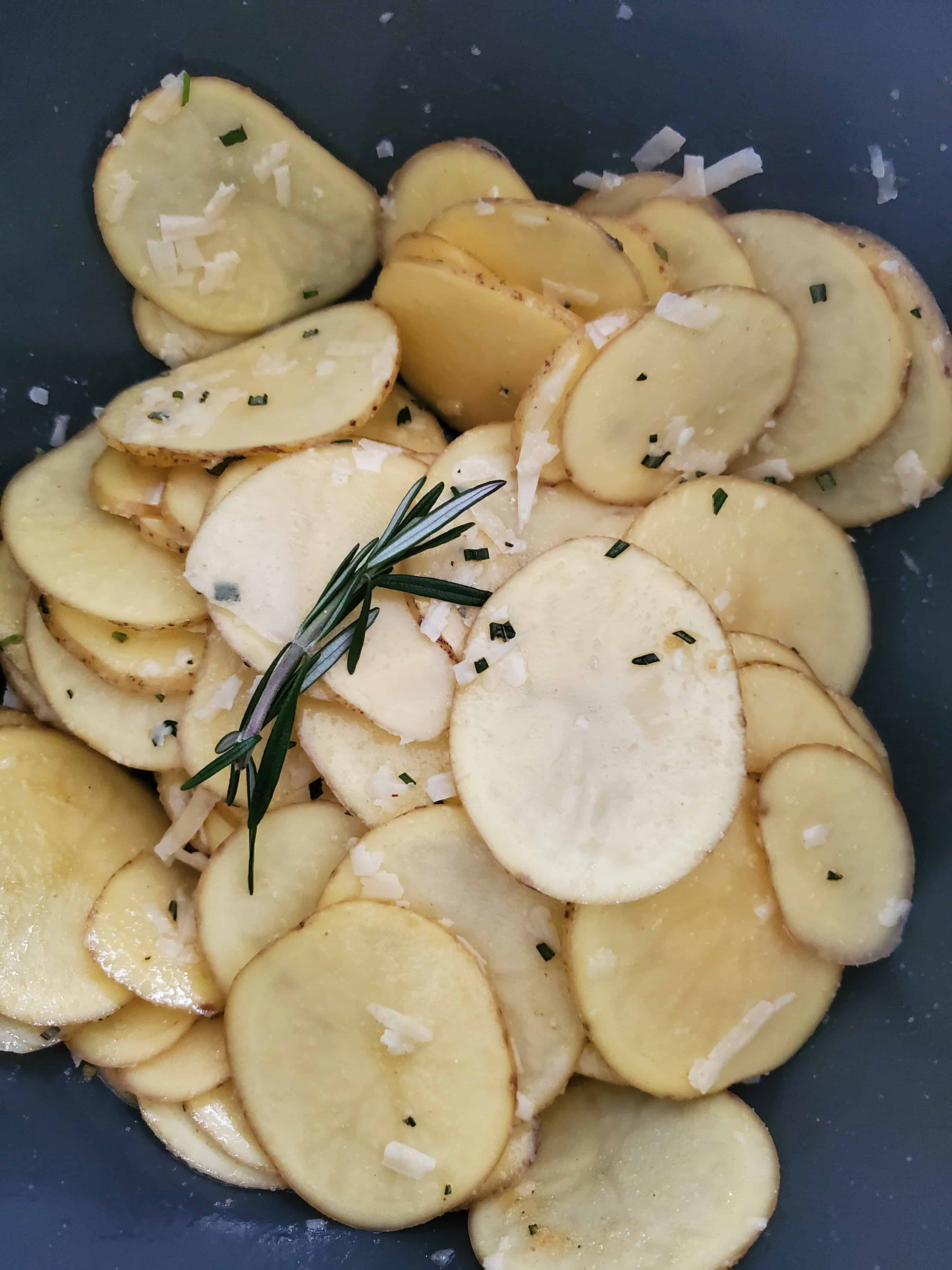 Bowl of sliced potatoes with rosemary, parmesan, and olive oil