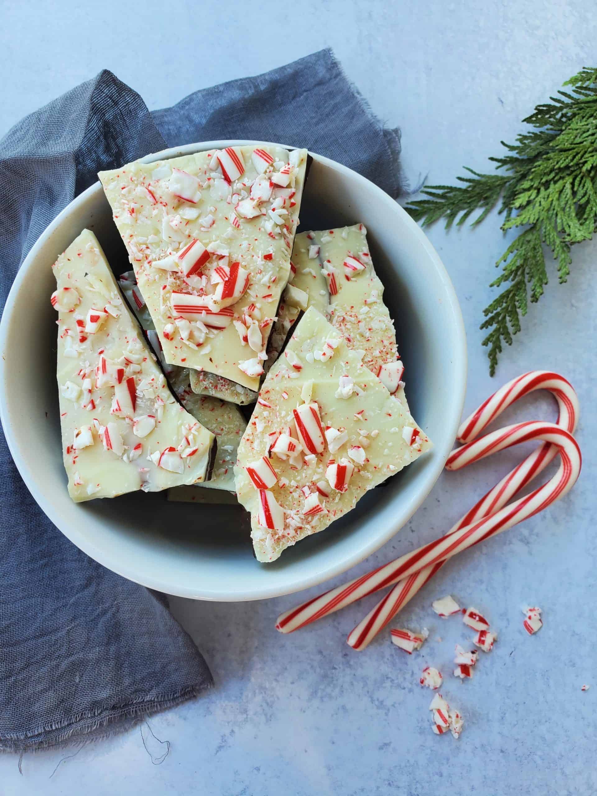 Peppermint Bark broken up in a bowl with candy canes and pine as decoration