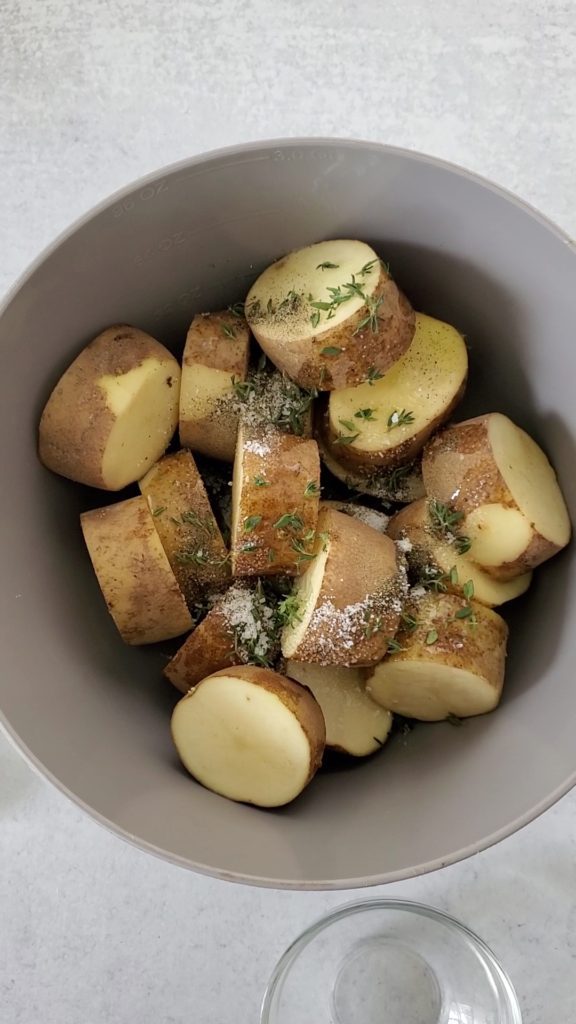 Potato discs in a large bowl with olive oil, butter, salt, pepper, and thyme