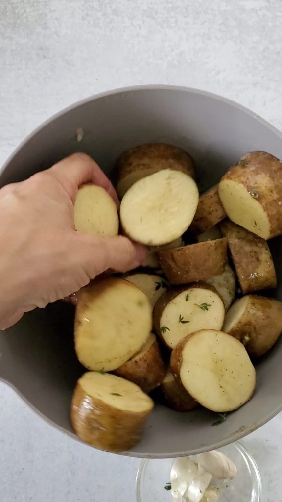 Large bowl with potato discs and spice and olive oil and butter all being mixed in with my hand