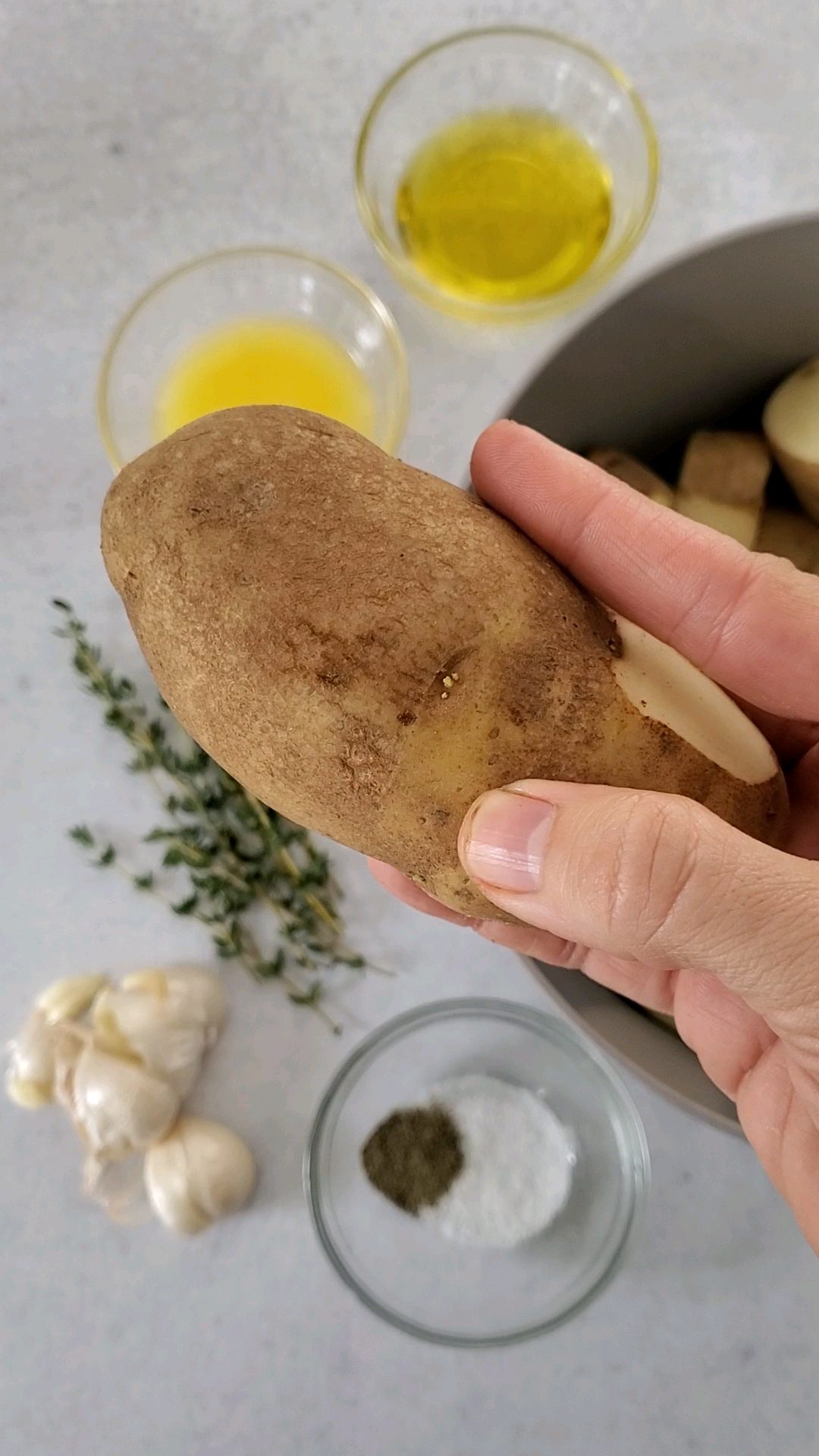 Whole Russett Potato up close with ingredients for melting potatoes - olive oil, butter, garlic, thyme