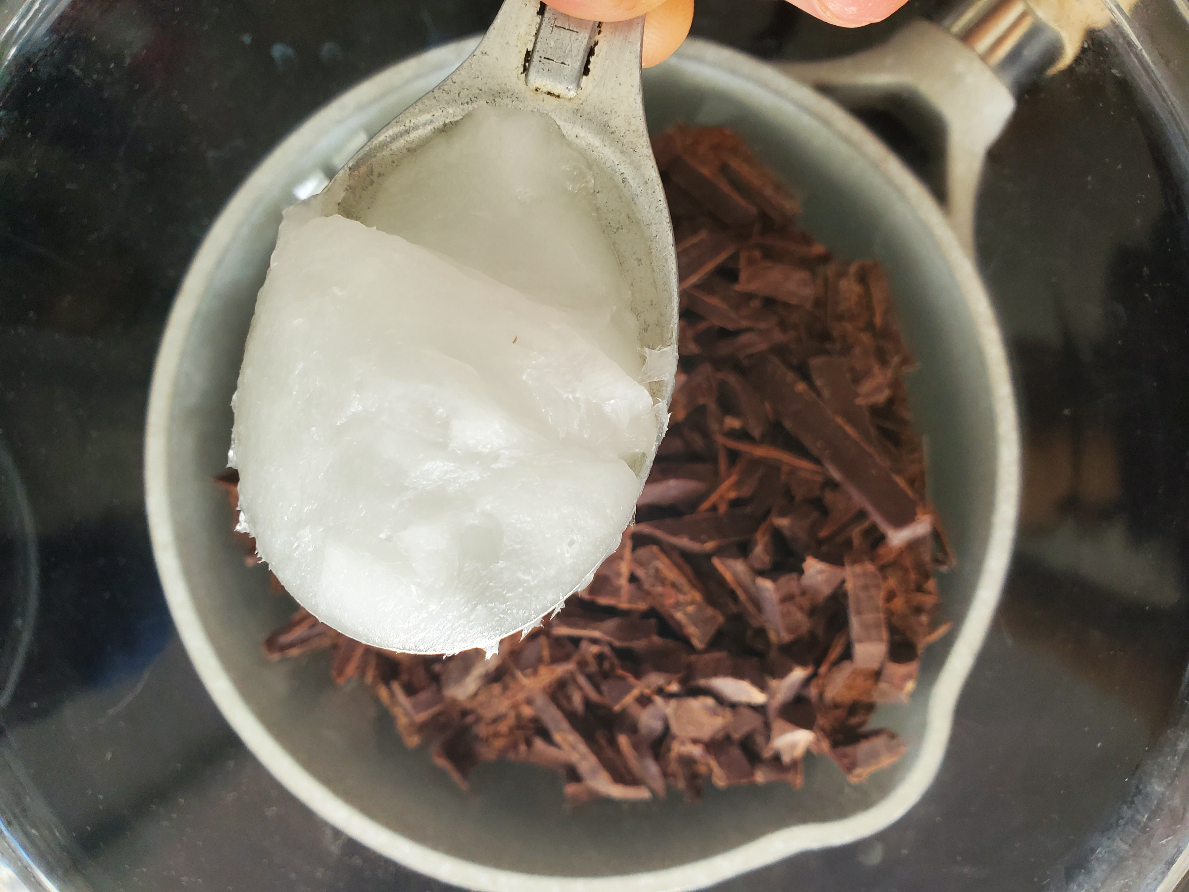 Coconut oil being added to a pot of chocolate to melt