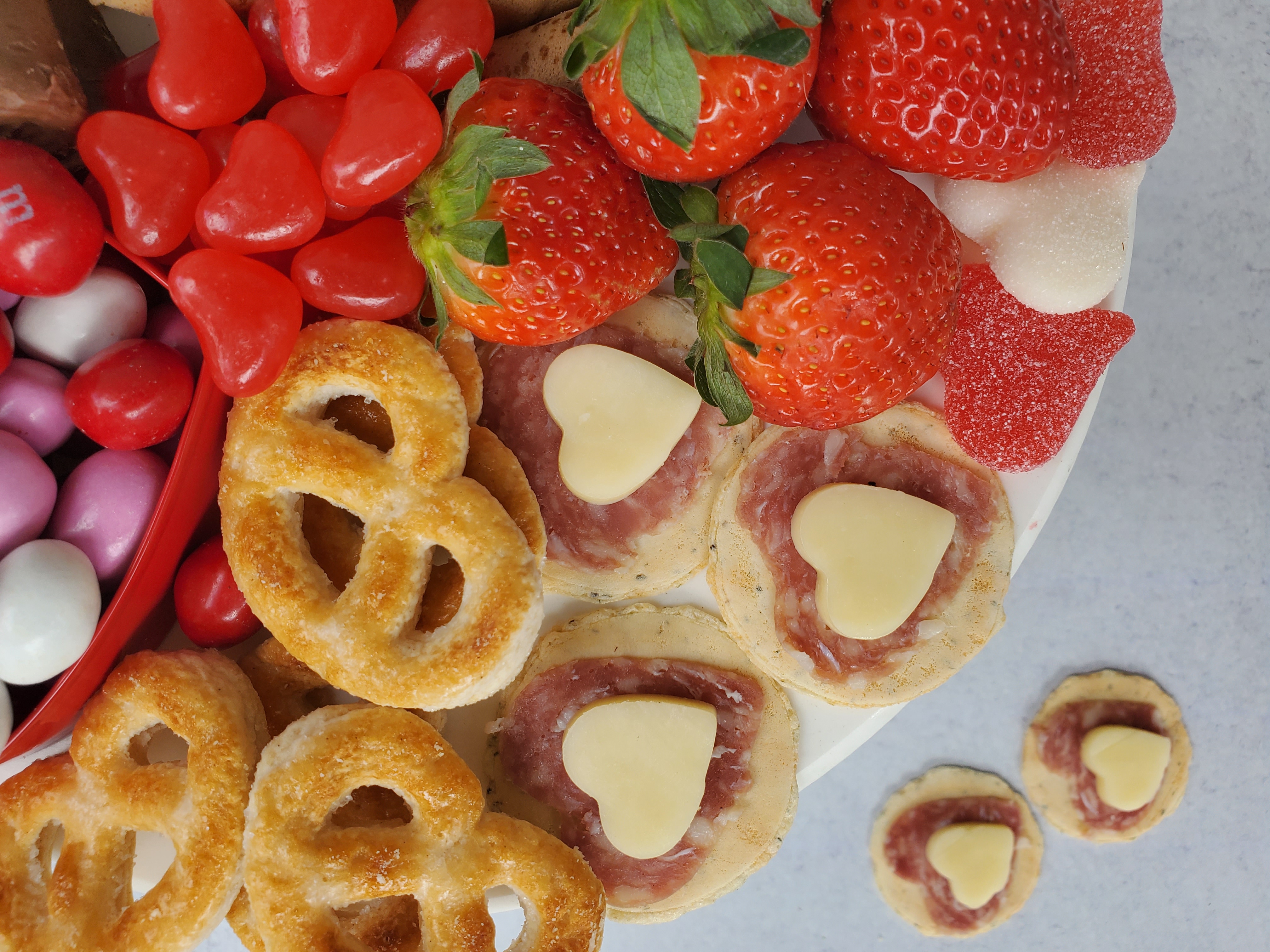 Close-up of a dessert board of candy, cookies, and cheese/salami heart shaped finger foods