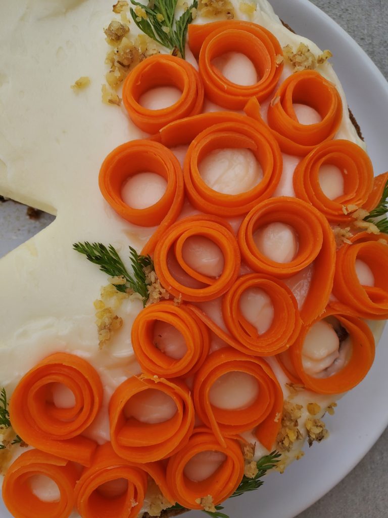 Close up carrot cake with carrot ribbons spiraled as a decoration on the cream cheese frosting