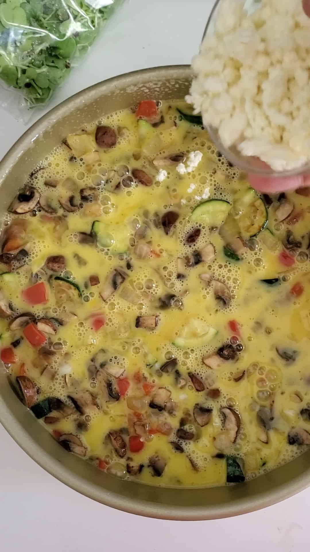 sprinkling cheese over uncooked frittata
