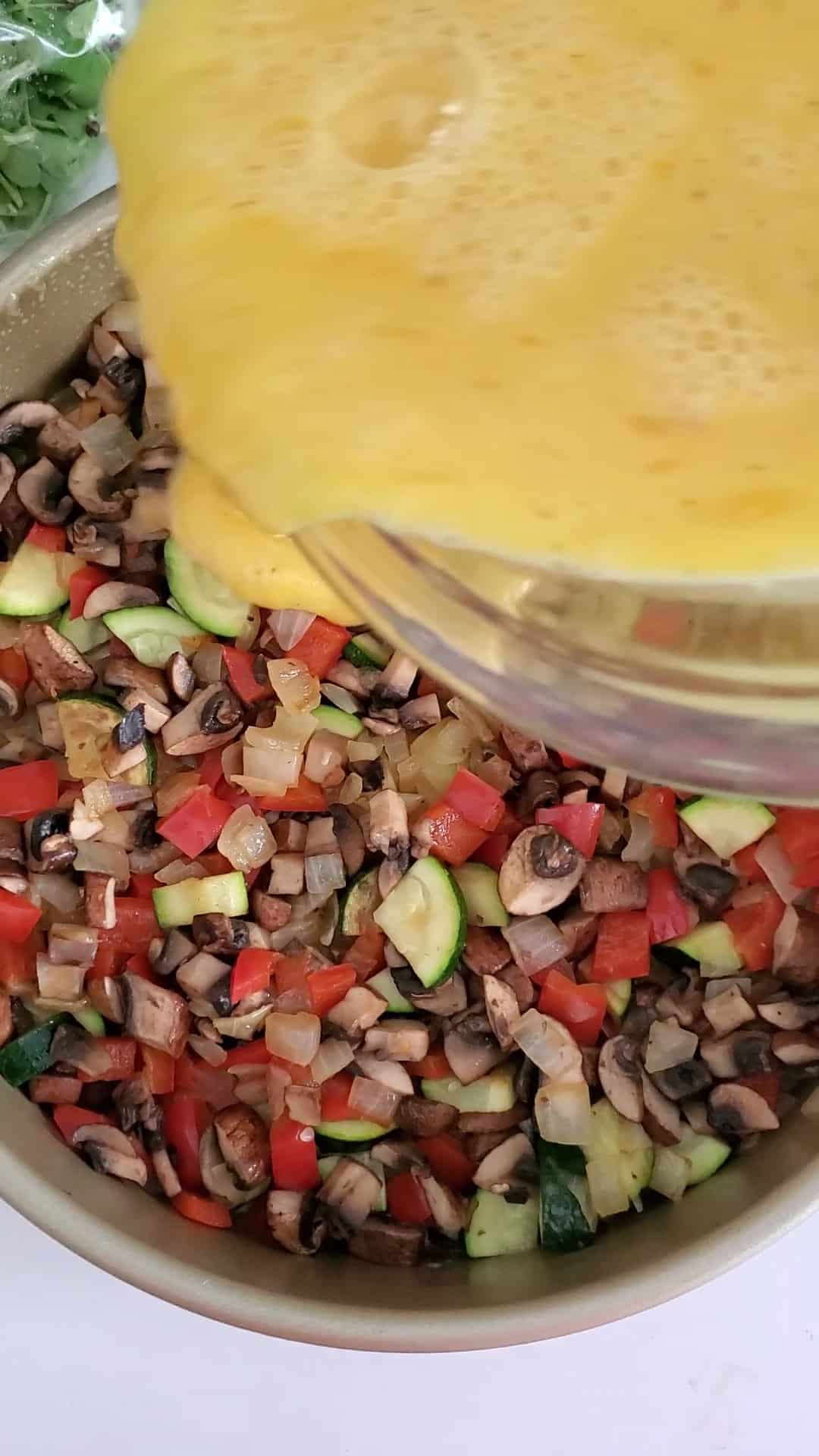 whisked eggs being poured into sautéed vegetables