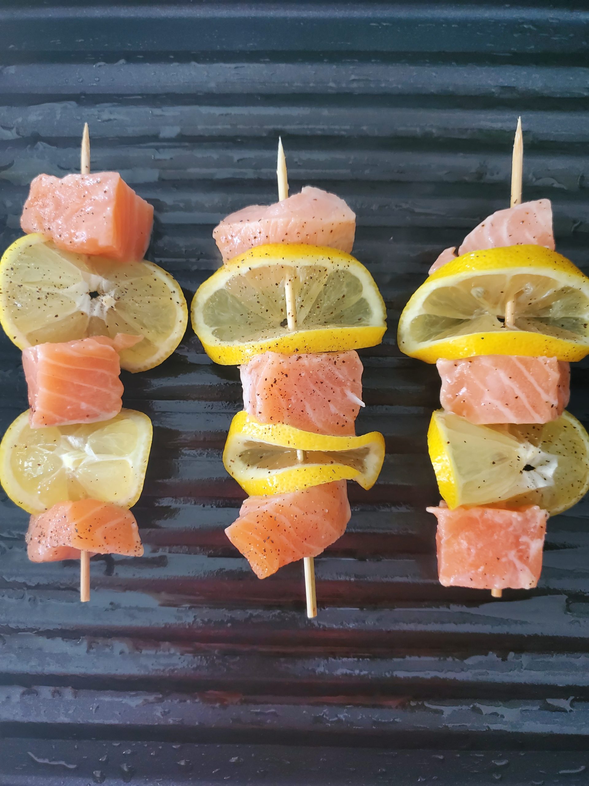 salmon skewers with lemon slices on a grill pan