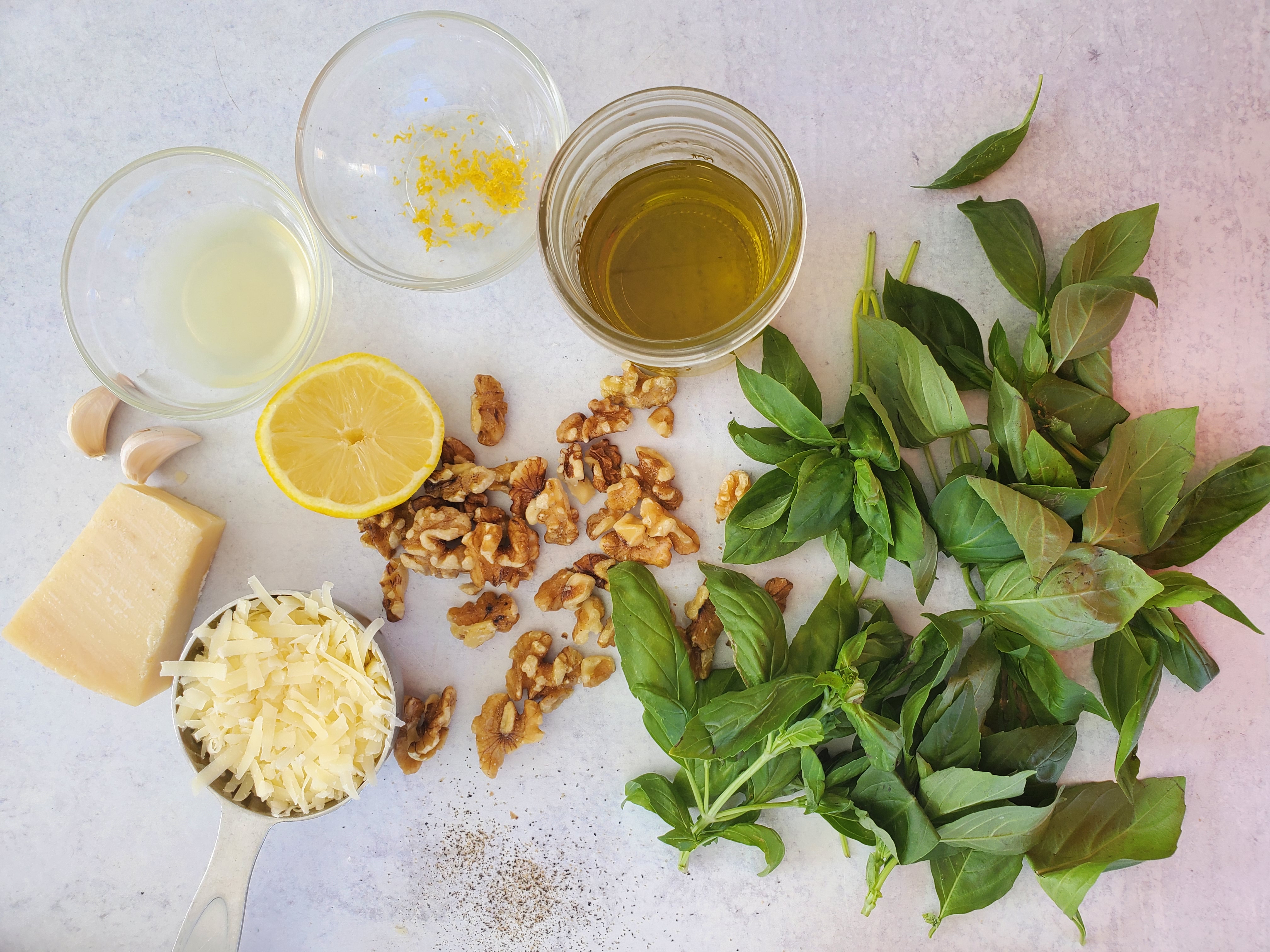 ingredients spread out for pesto - basil, olive oil, lemon, walnuts, garlic, parmesan cheese