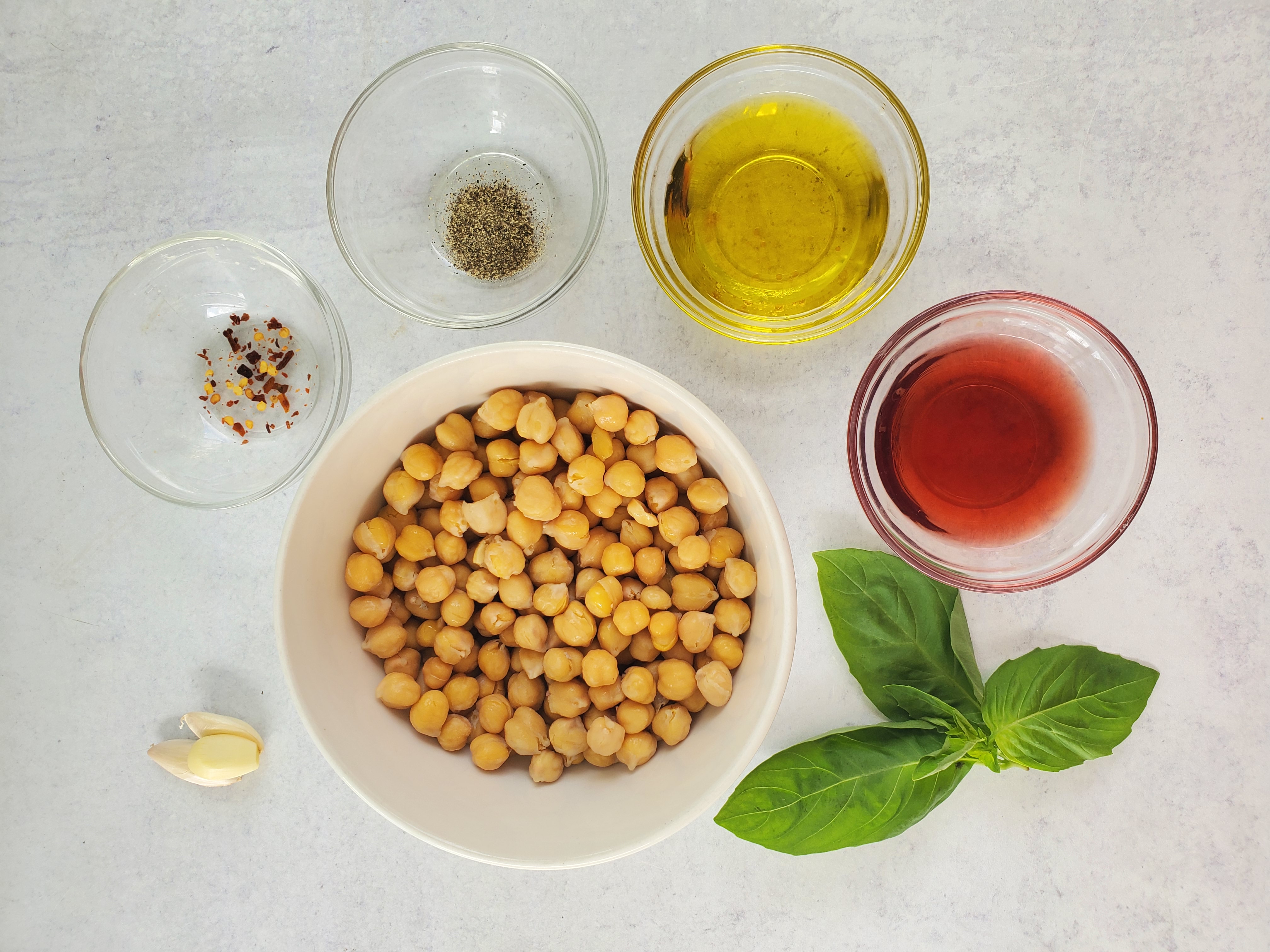 ingredients laid out for marinating chickpeas:  chickpeas, basil, red wine vinegar, olive oil, black pepper, garlic, red pepper flakes