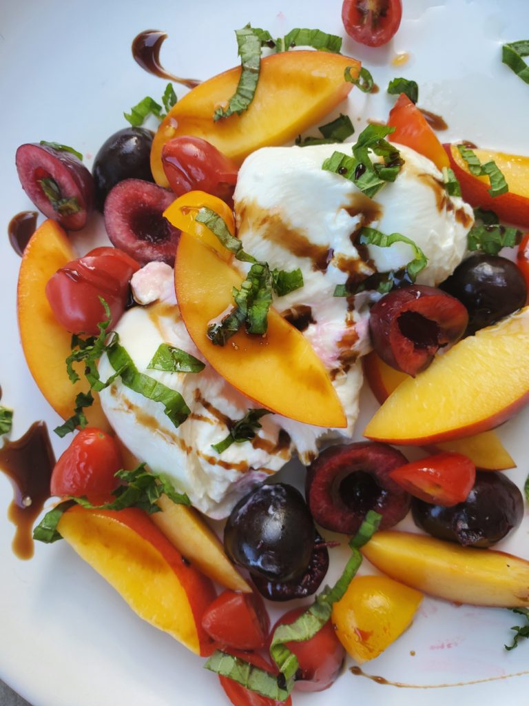 Plate with burrata cheese, nectarine, cherries, mint, basil, and a drizzle of balsamic glaze