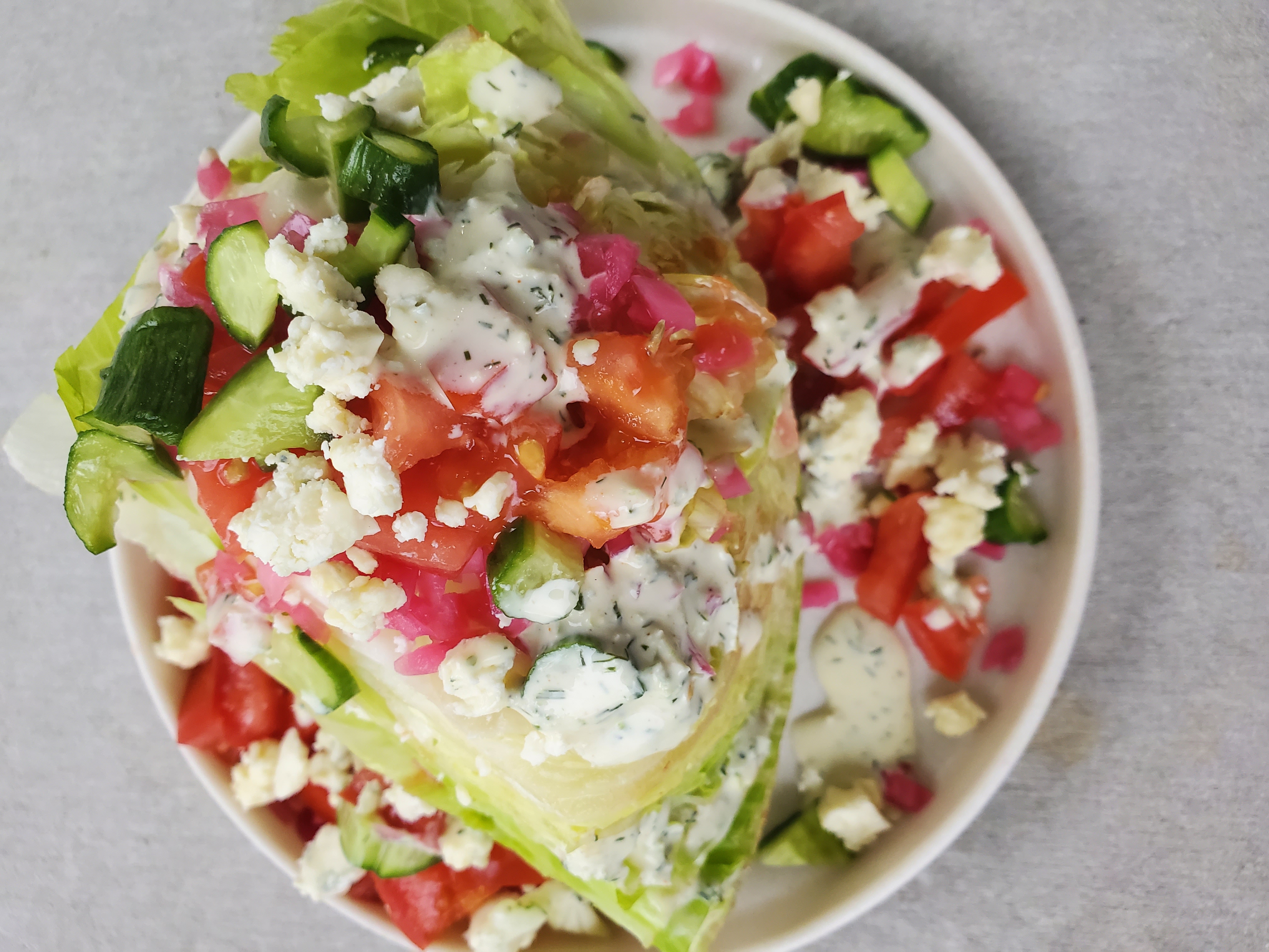 wedge of iceberg lettuce plates with tomatoes, cucumber, pickled red onion, and blue cheese dressing