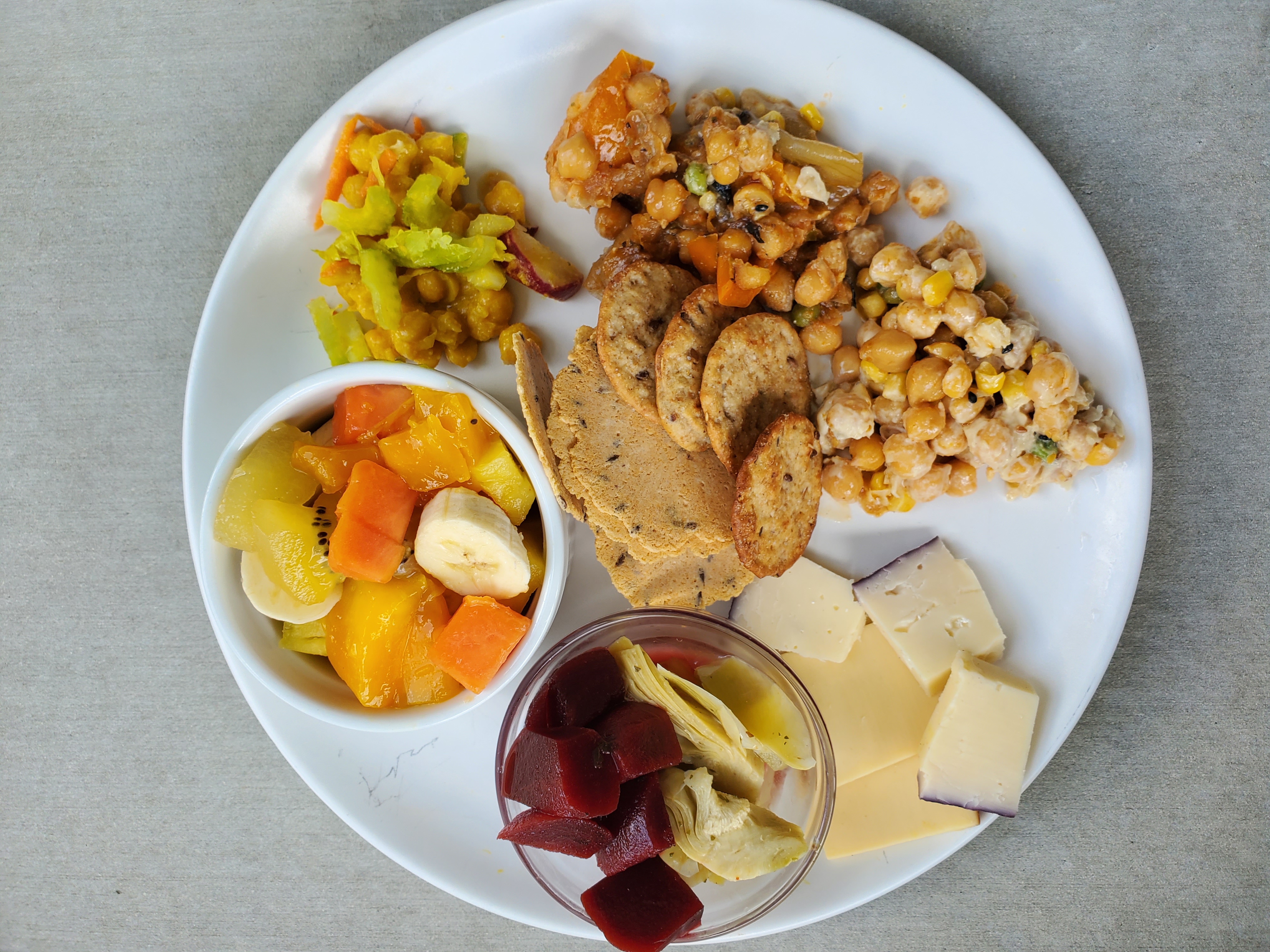 Plate of chickpea salads, fruit, marinated beets and artichokes, cheese, and fruit salad