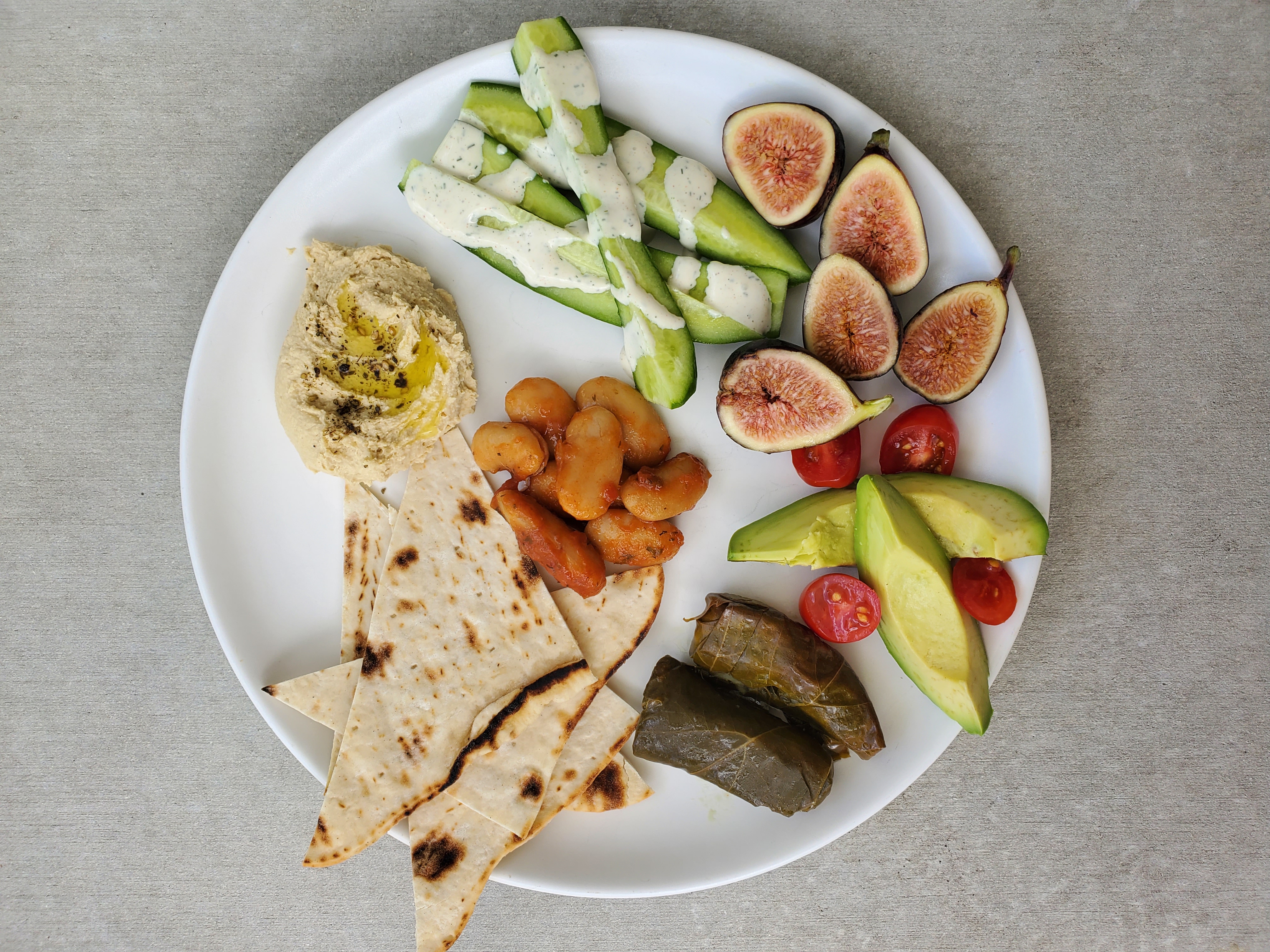 Plate of snack foods: butter beans, grape leaves, hummus, cucumbers, avocado, and figs