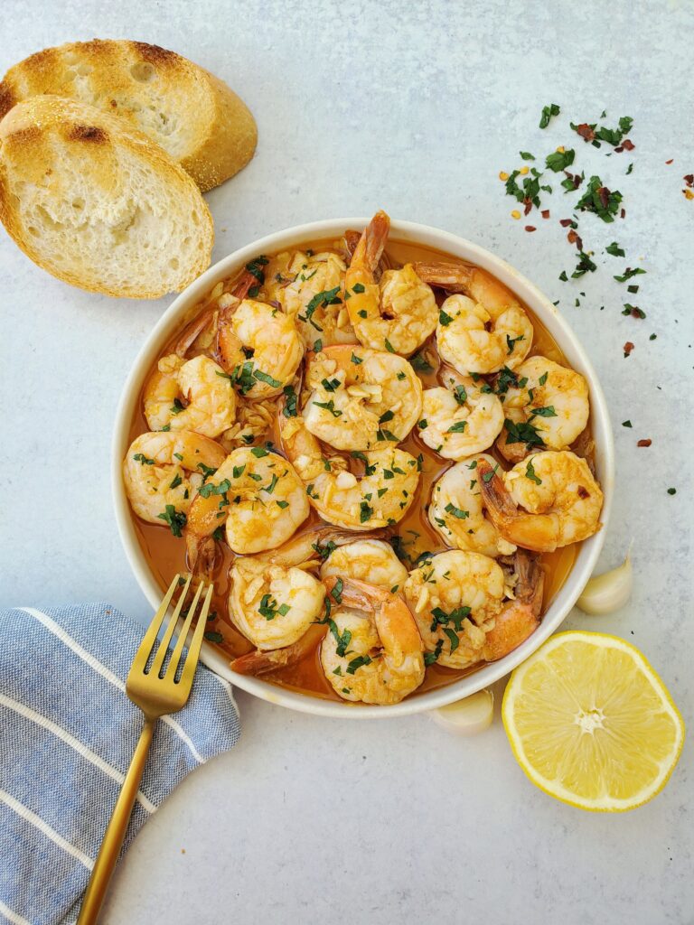 Gambas al ajillo aka garlic shrimp on a plate with a fork and crusty bread