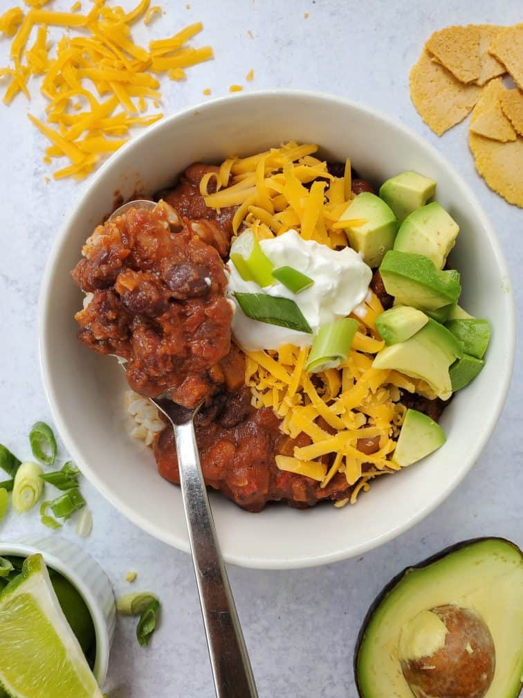 bowl of vegetarian chili with avocado, cheese, and sour cream as toppings