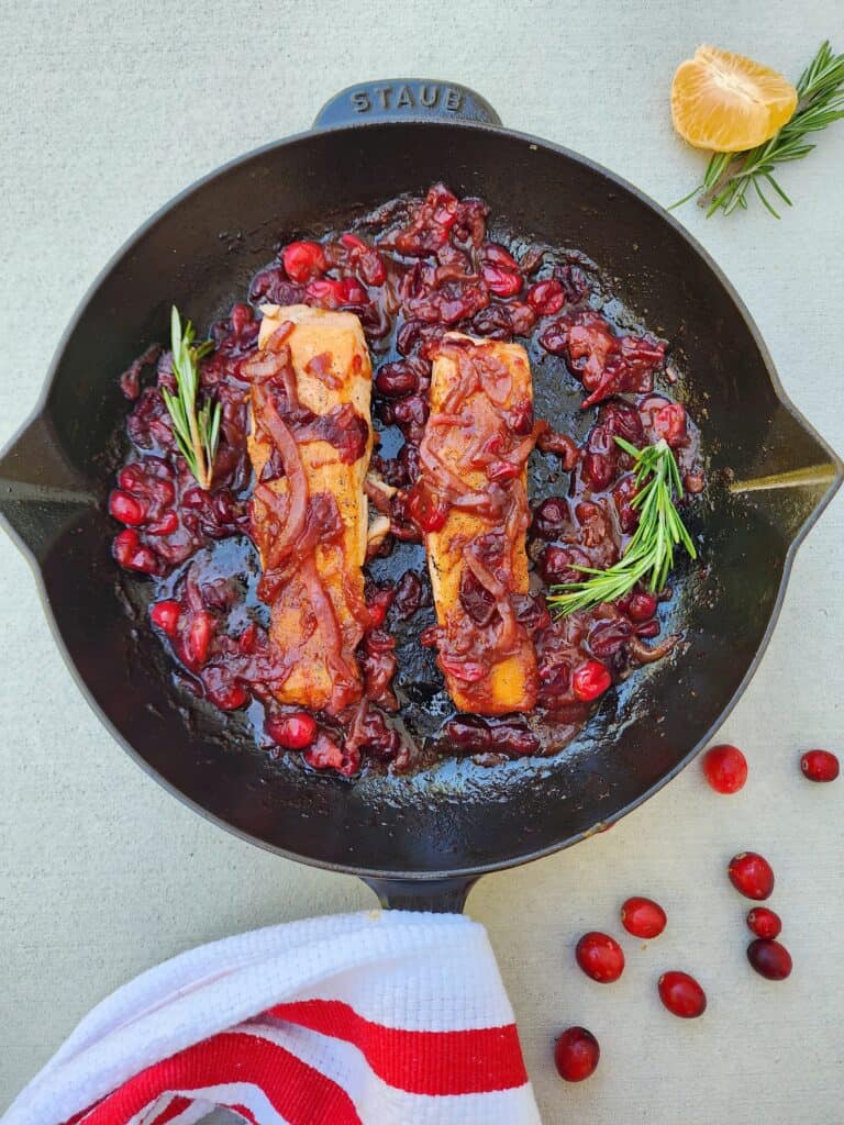 cast-iron pan with 2 salmon fillets in a cranberry, orange, rosemary sauce