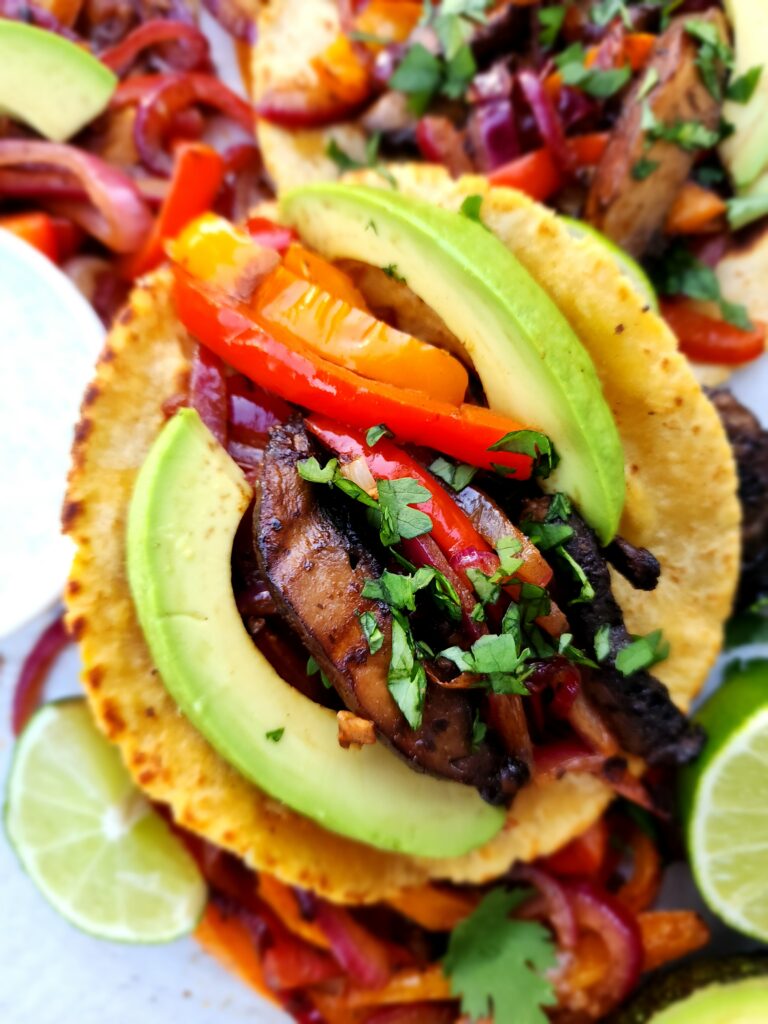 Close up picture of a portobello, bell pepper, red onion, and avocado fajita on a corn tortilla