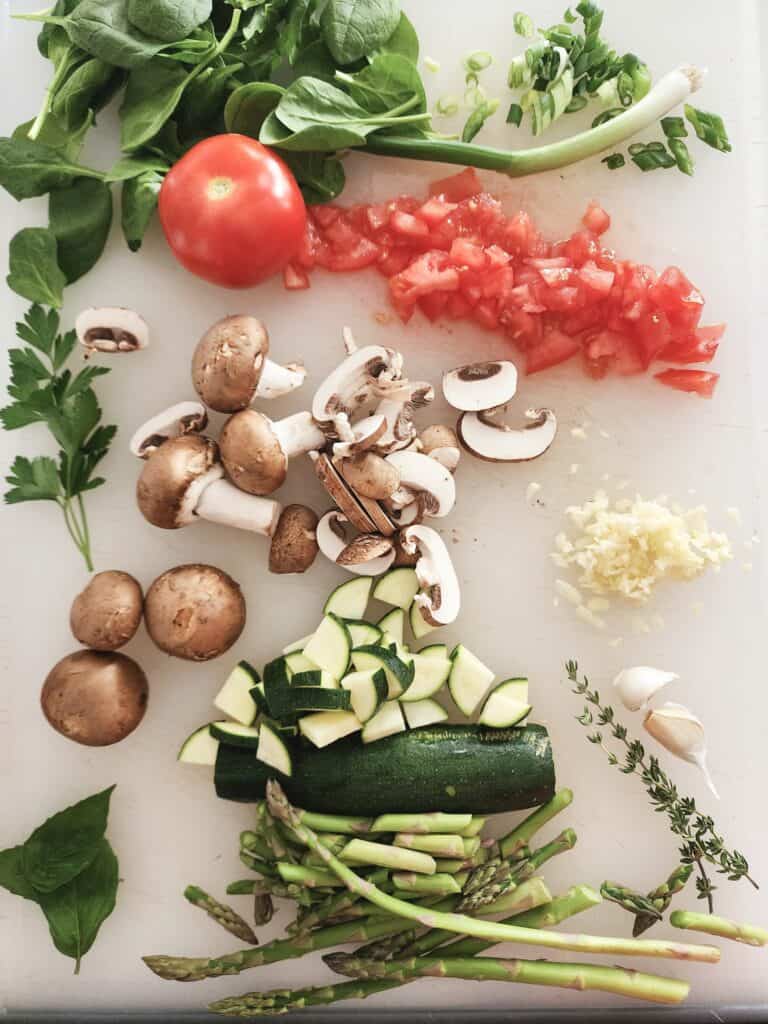 cutting board with tomato, mushrooms, zucchini, green onion, garlic, spinach