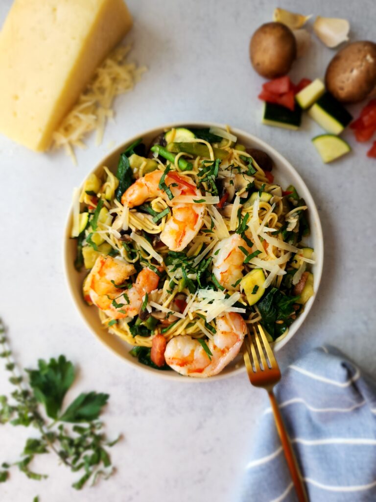 plate filled with pasta, veggies, and shrimp with parmesan cheese