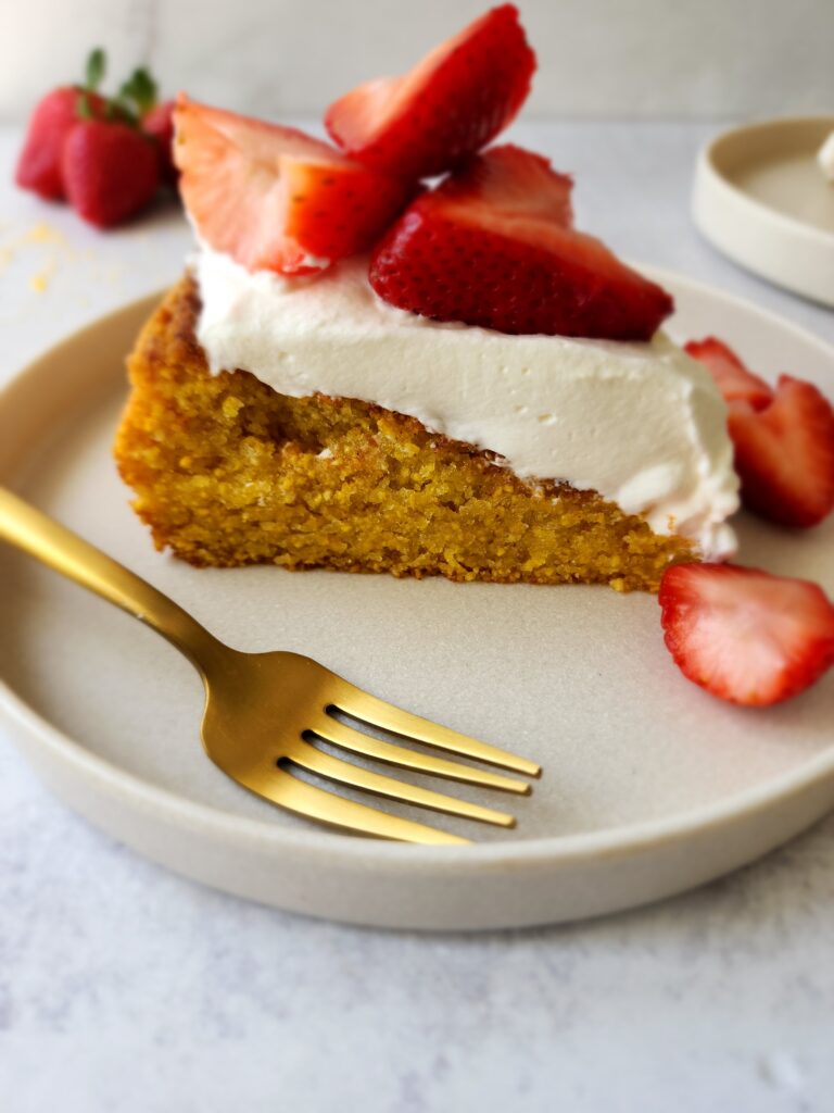 slice of olive oil cake from the side with whipped cream and strawberries
