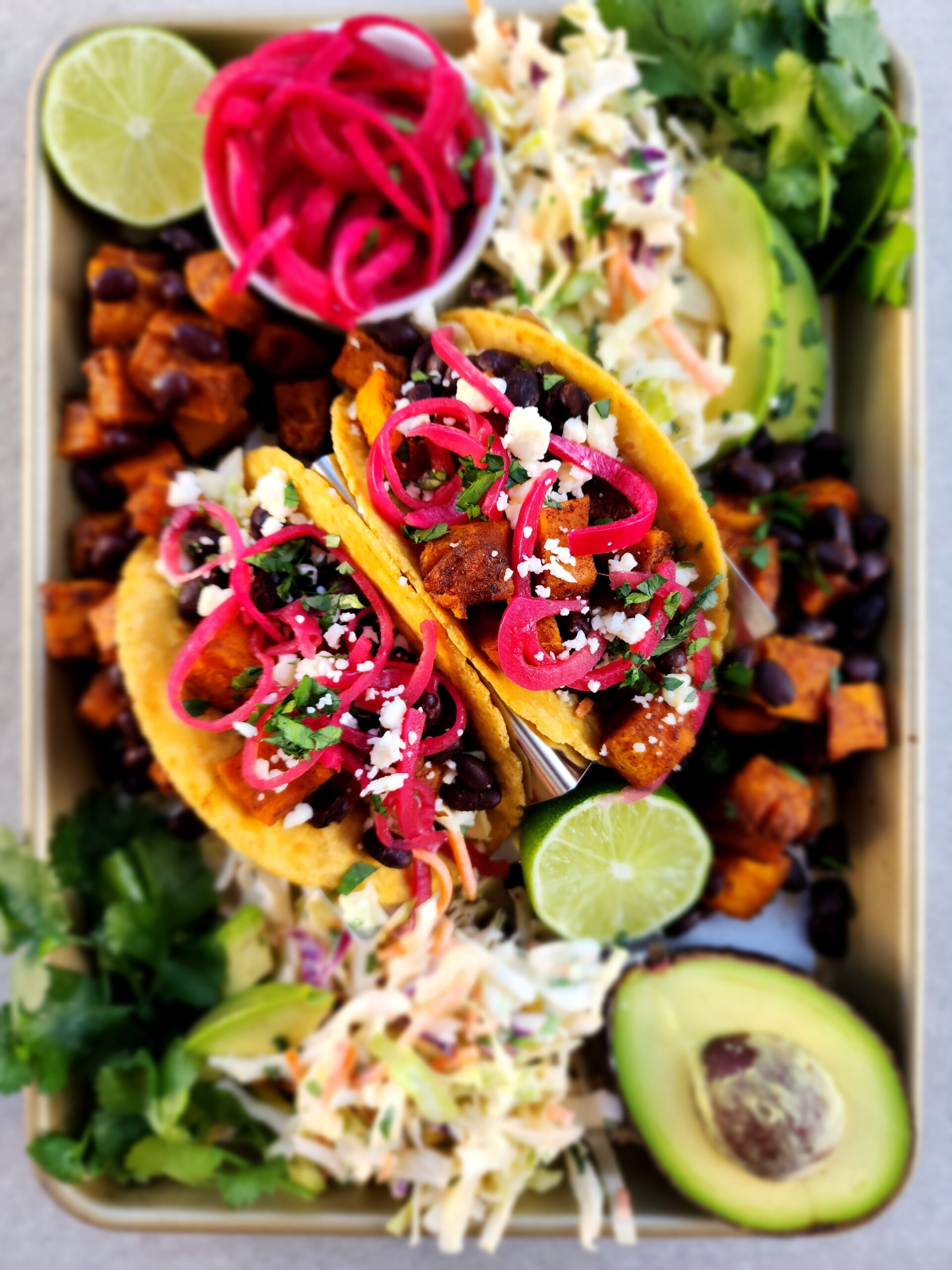 Roasted Butternut Squash and Black Bean Tacos on a sheet tray with avocado, coleslaw, pickled onions, and lime