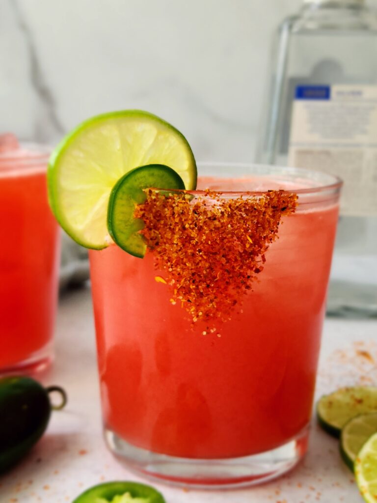 Close-up shot of a watermelon margarita with tajin rim, slice of lime and jalapeno