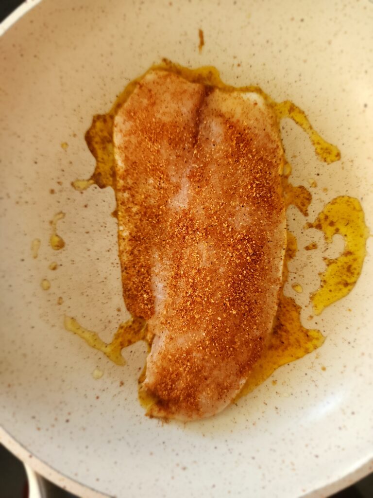 Sauté pan with white fish starting to cook with blackened seasoning