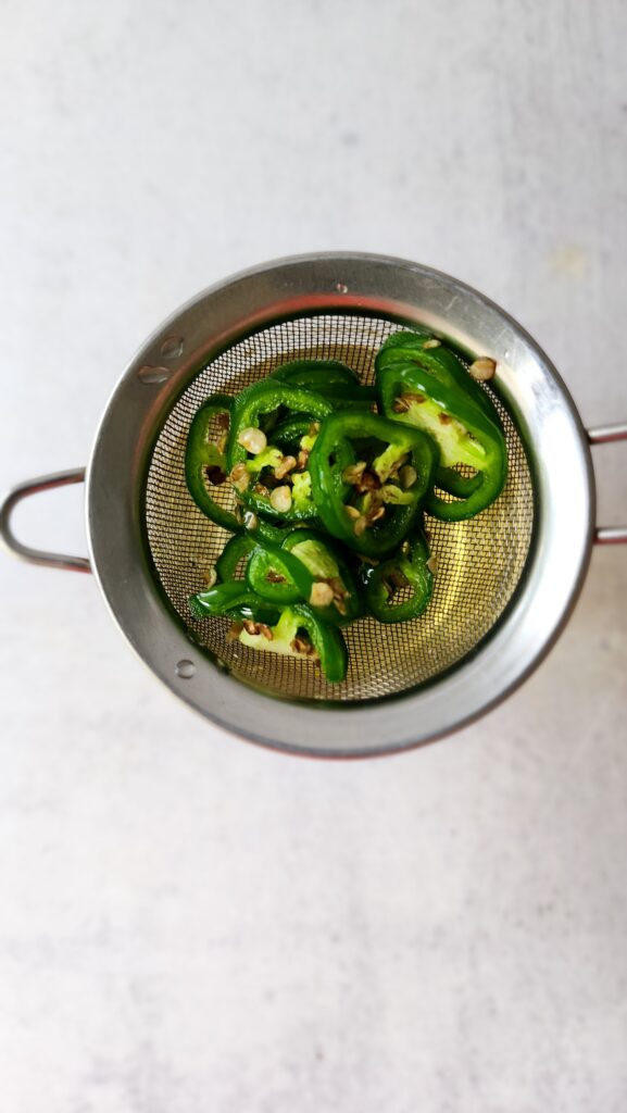 jalapeños in a strainer sitting on top of a mason jar