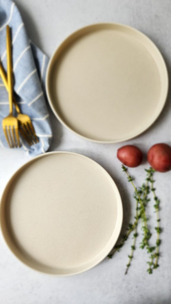 2 empty plates with forks, thyme, and potatoes as props for decoration