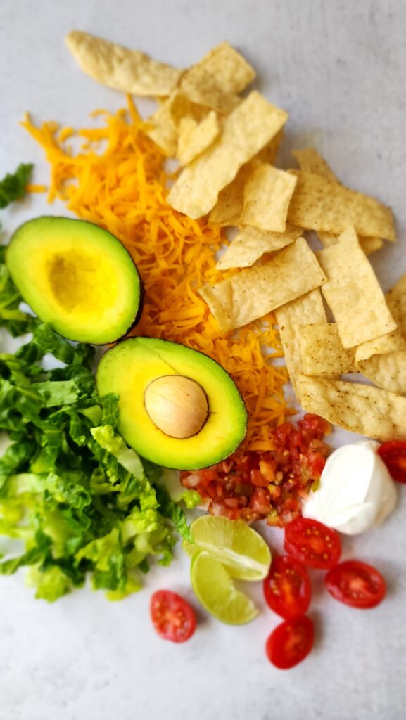 toppings for taco salad - lettuce, pico de gallo, sour cream, shredded cheese, avocado, and tortilla chips