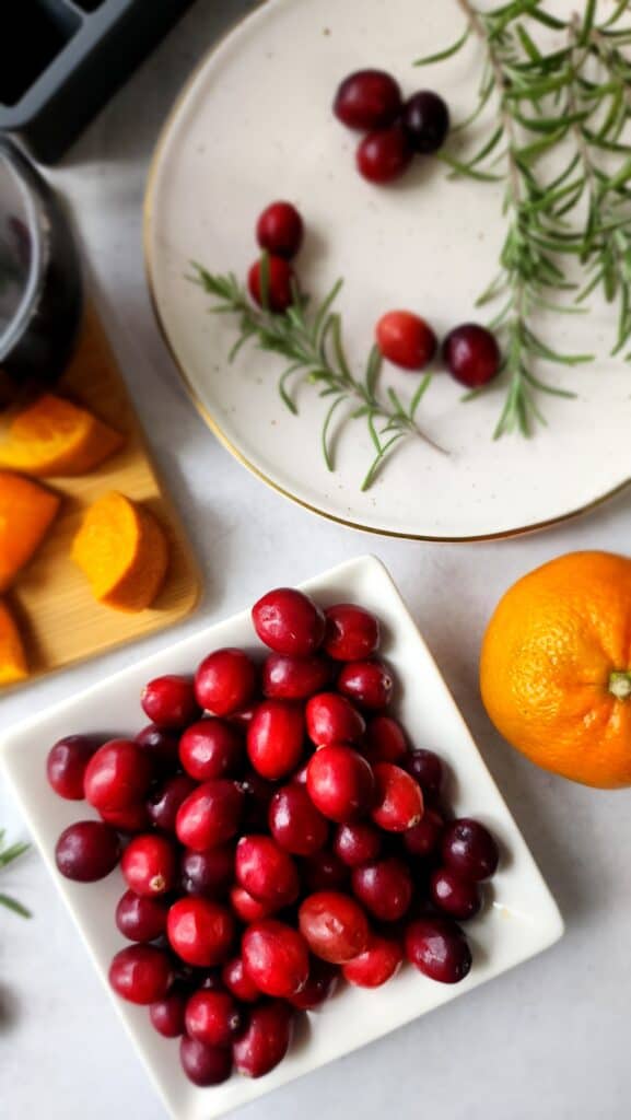 bowl of cranberries, oranges cut into triangles, and fresh rosemary on a plate