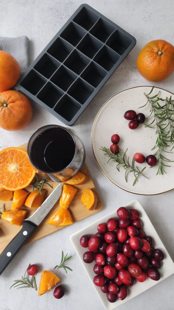 Top shot of ice cube tray with rosemary, orange slices, cranberries, and pomegranate juice