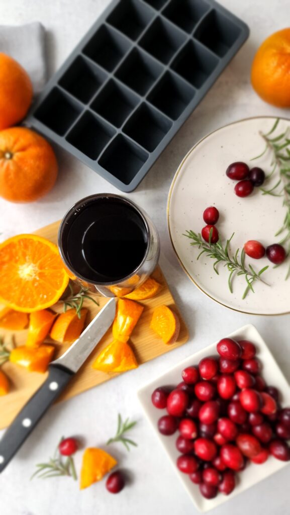 Ice cube tray empty, with orange slices, cranberries, pomegranate, and rosemary to add in